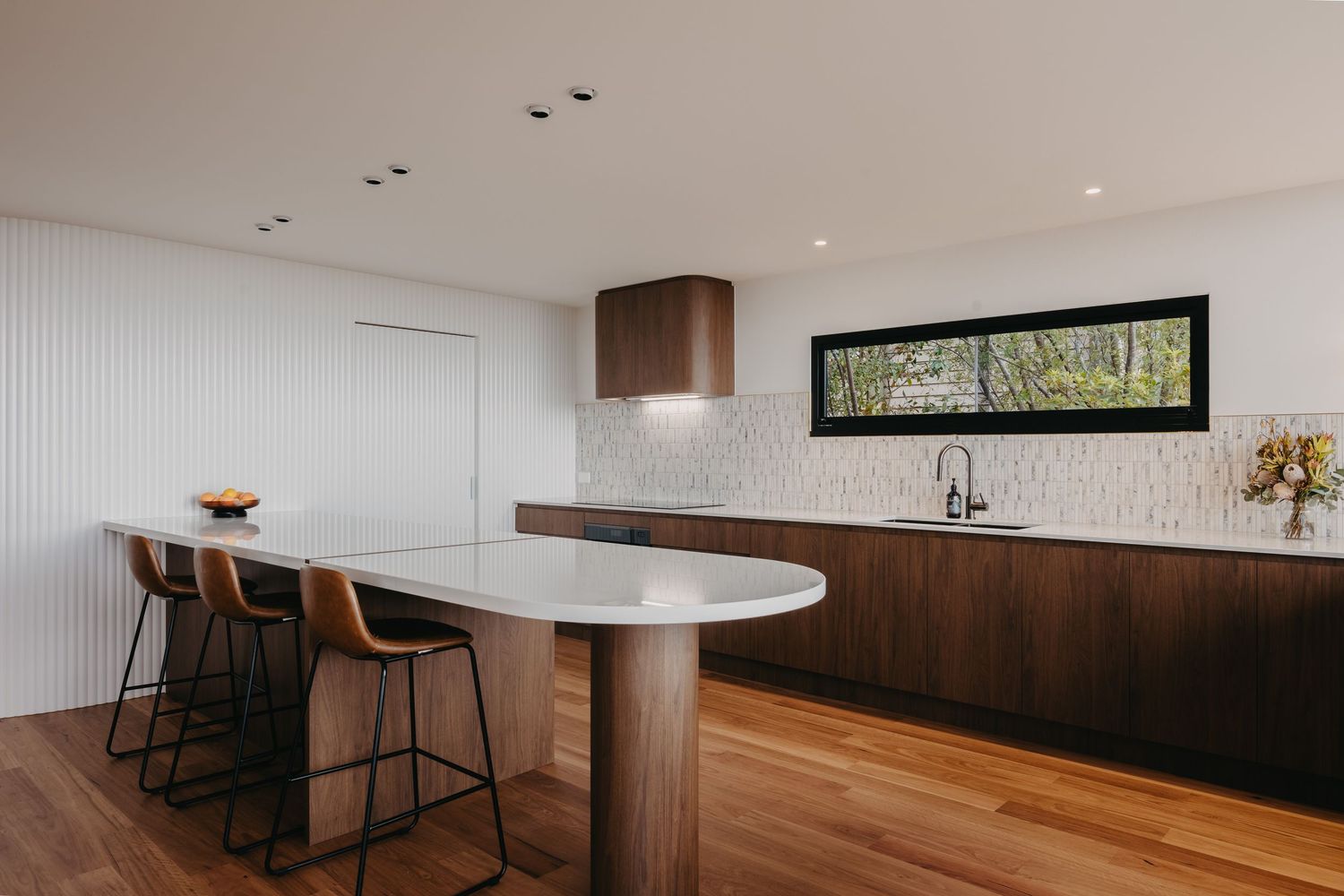 Minimalist kitchen design with walnut cabinets, white countertop island, leather bar stools, and tile backsplash.