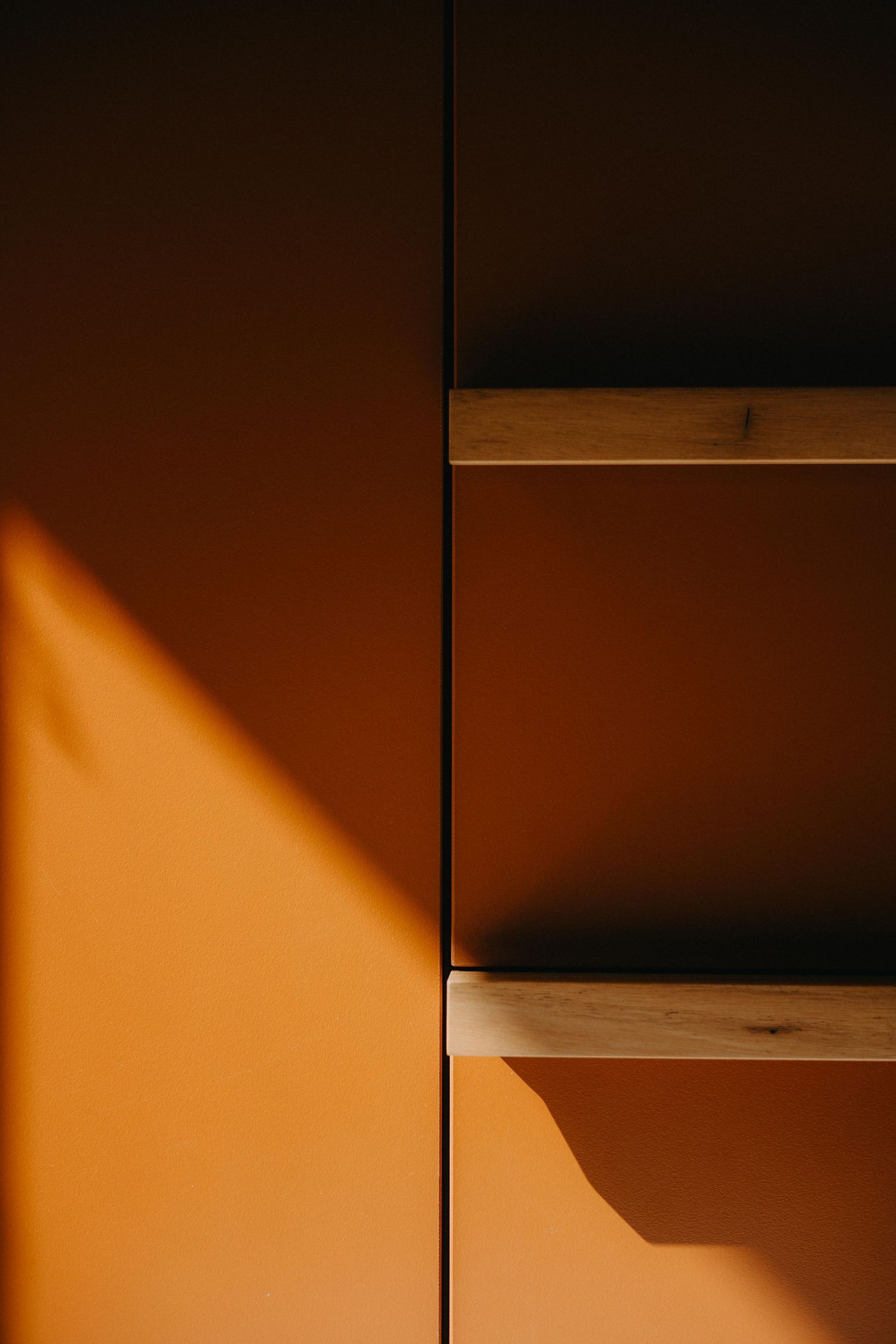 Close-up of orange cabinetry with timber shelves casting dramatic shadows in warm sunlight.