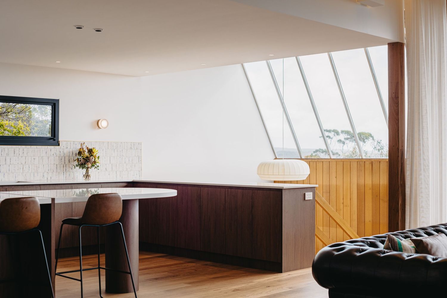 Modern open-plan kitchen with dark walnut cabinetry, timber ceiling detail, large skylight, and leather sofa.