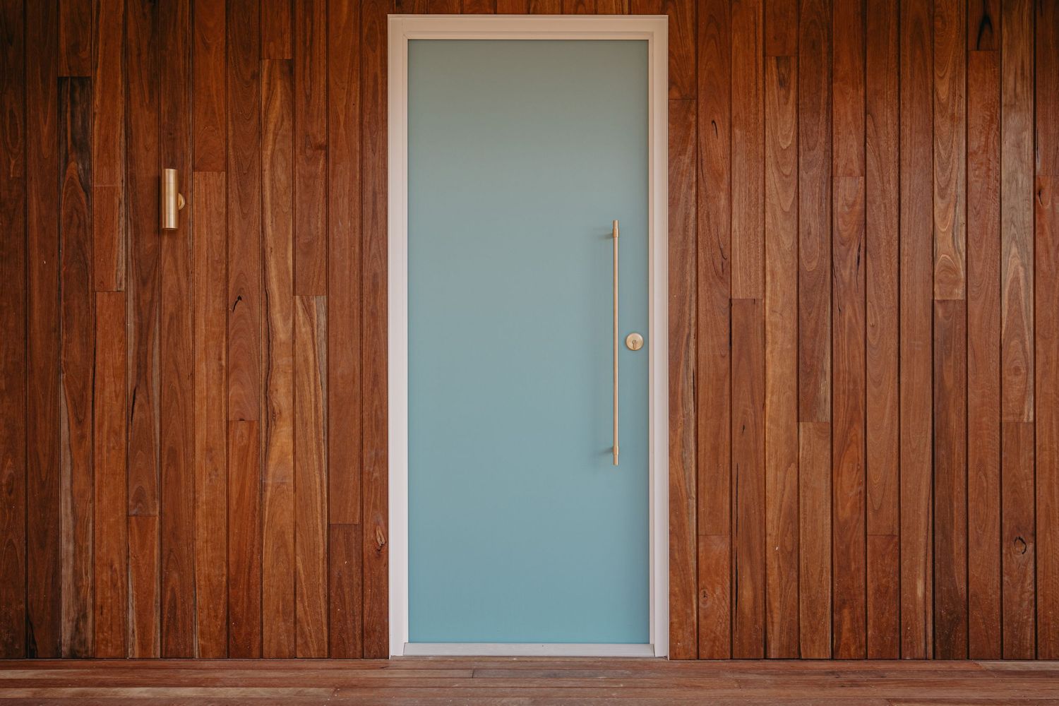 Teal front door with tall brass pull handle set against rich dark timber horizontal wood cladding exterior wall.