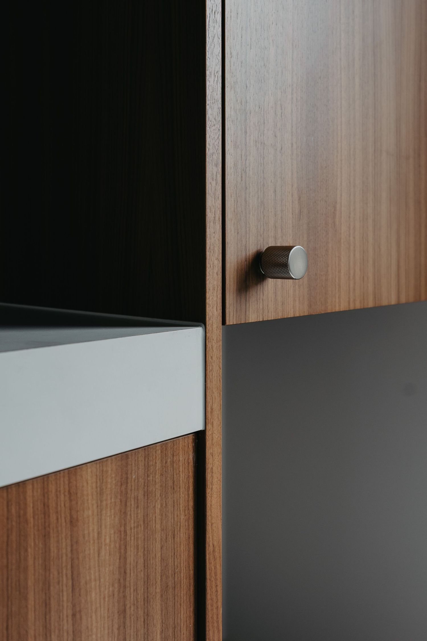 Close-up of walnut cabinet door with cylindrical brushed metal knob and dark panel detail.