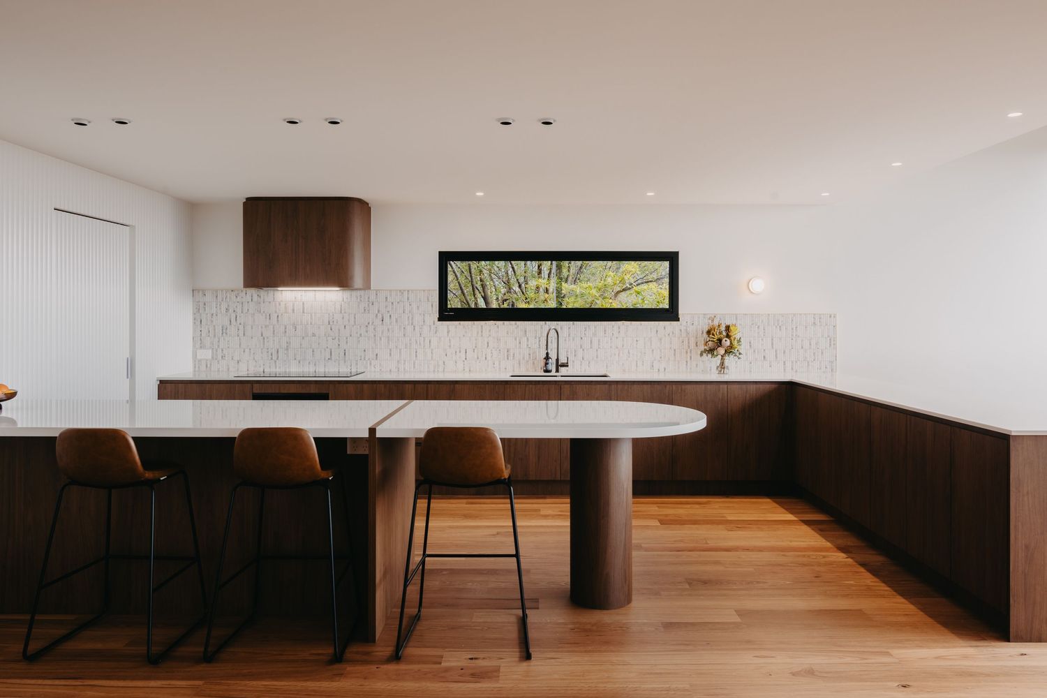 Modern kitchen with dark walnut cabinets, white marble island, bar stools, and textured tile backsplash.