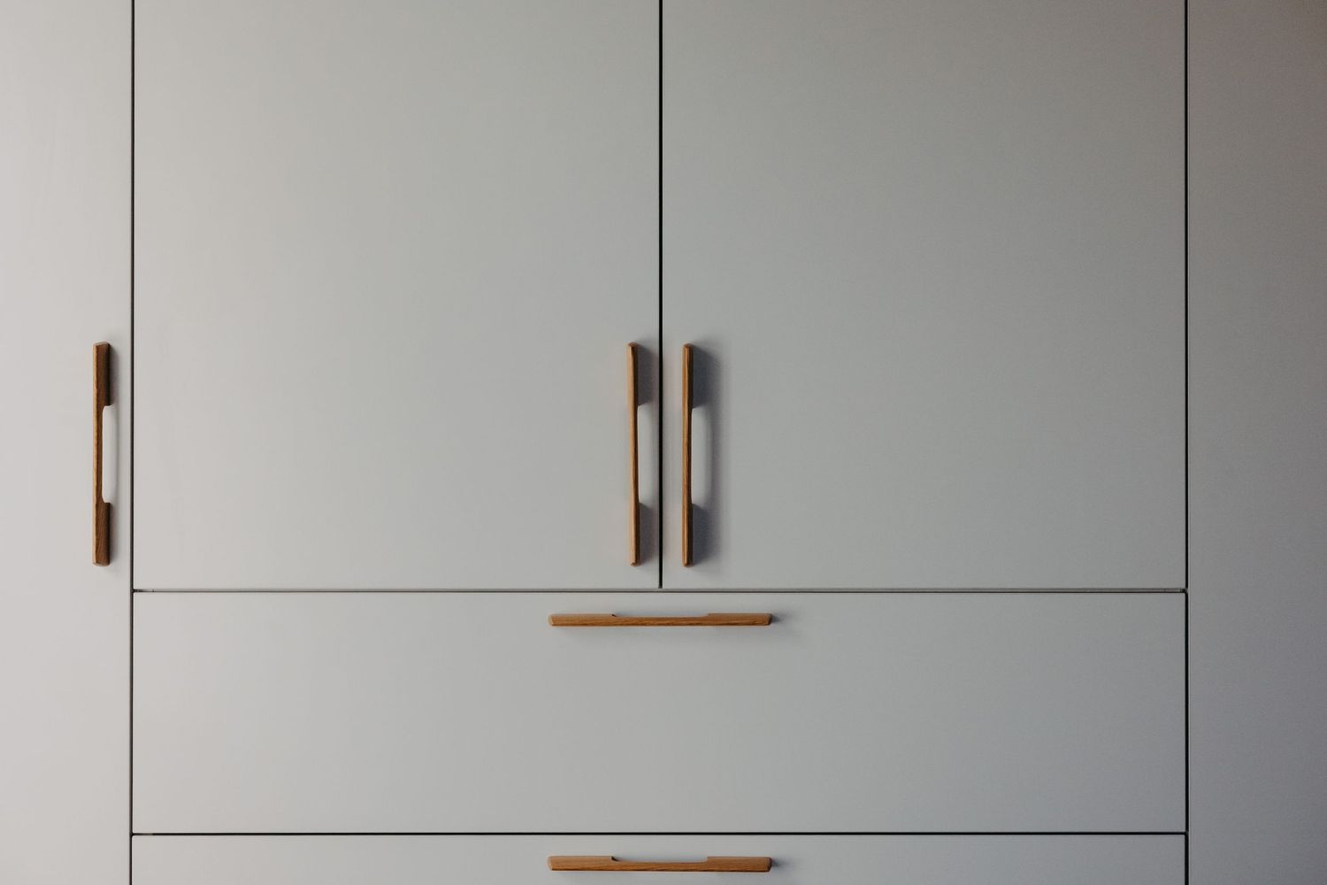 Modern light gray wardrobe with sleek wooden handles on cabinet doors and drawers.