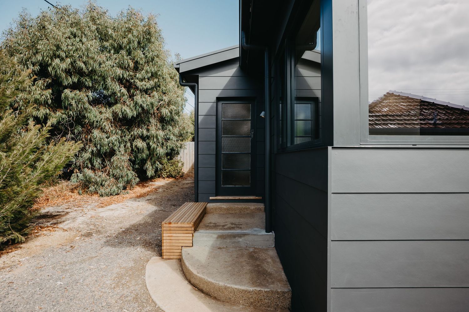 Dark charcoal clad home exterior with timber entry steps and black framed glass front door.