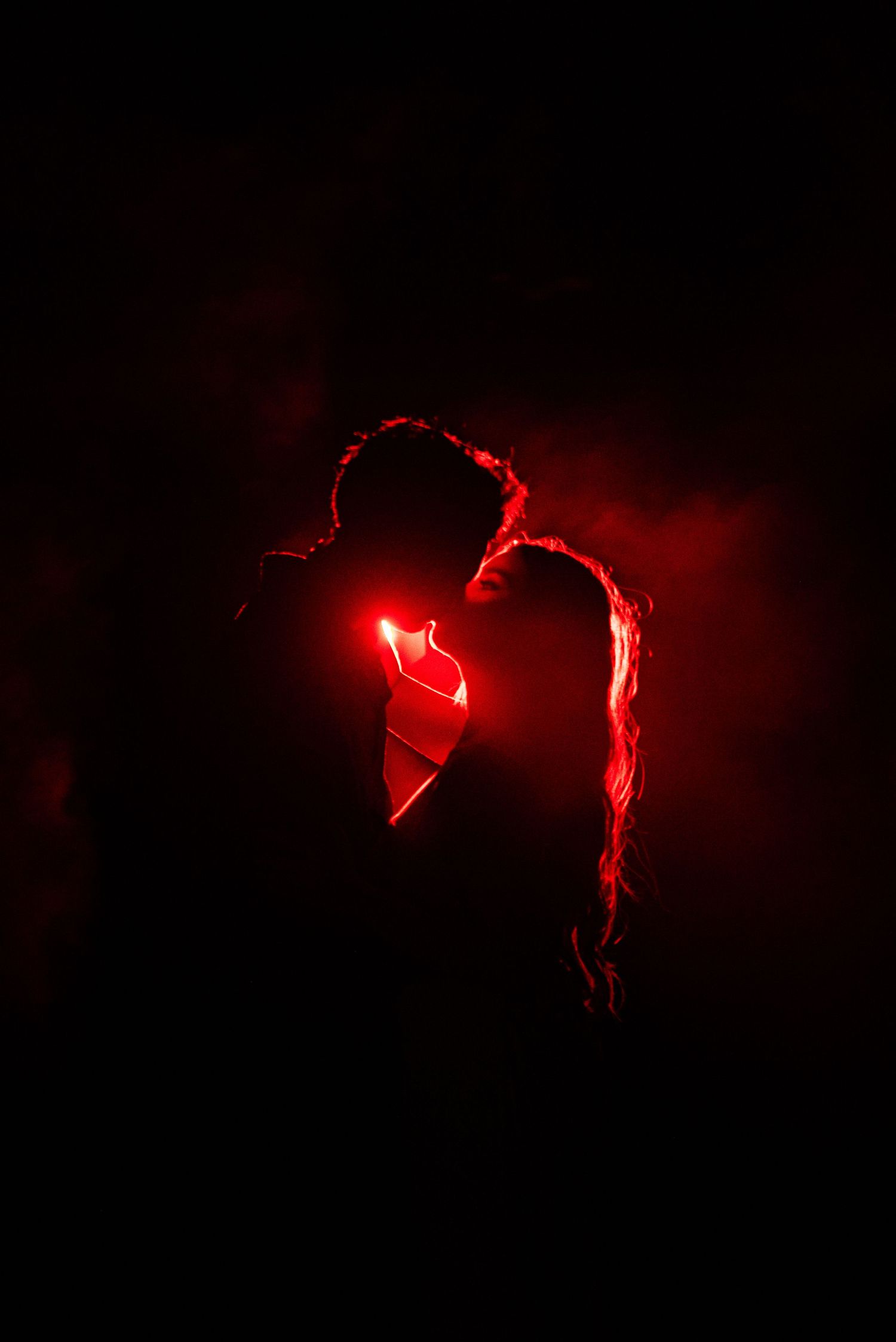 Romantic couple silhouette with glowing red heart light in dark moody atmosphere.