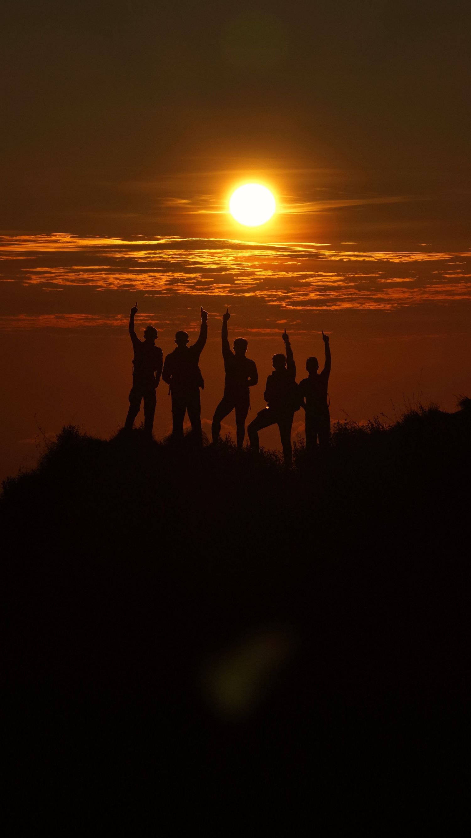 Silhouettes of five people with raised arms celebrating on a hilltop against a vibrant orange sunset sky.