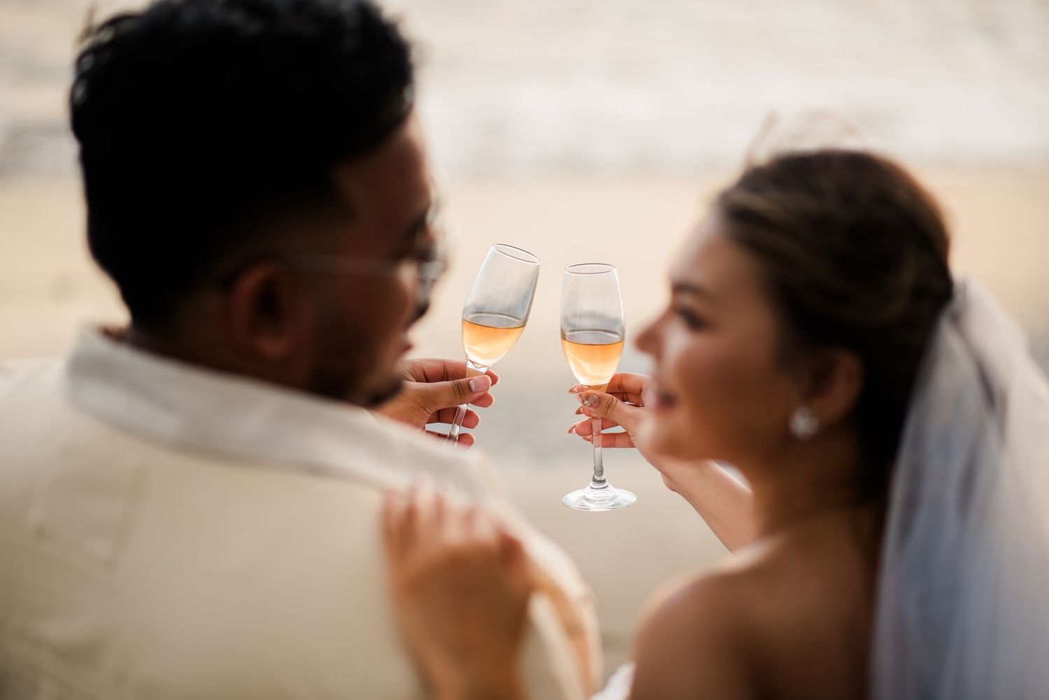 Newlywed couple toasting with champagne glasses on their wedding day, bride in veil smiling at groom.