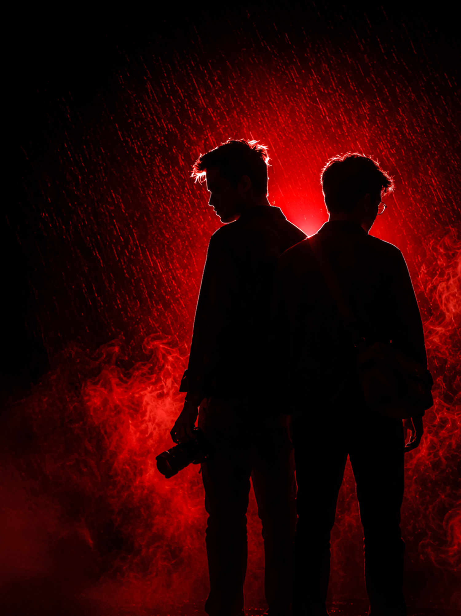 Two silhouetted figures stand against a dramatic red smoky background, one holding a camera.