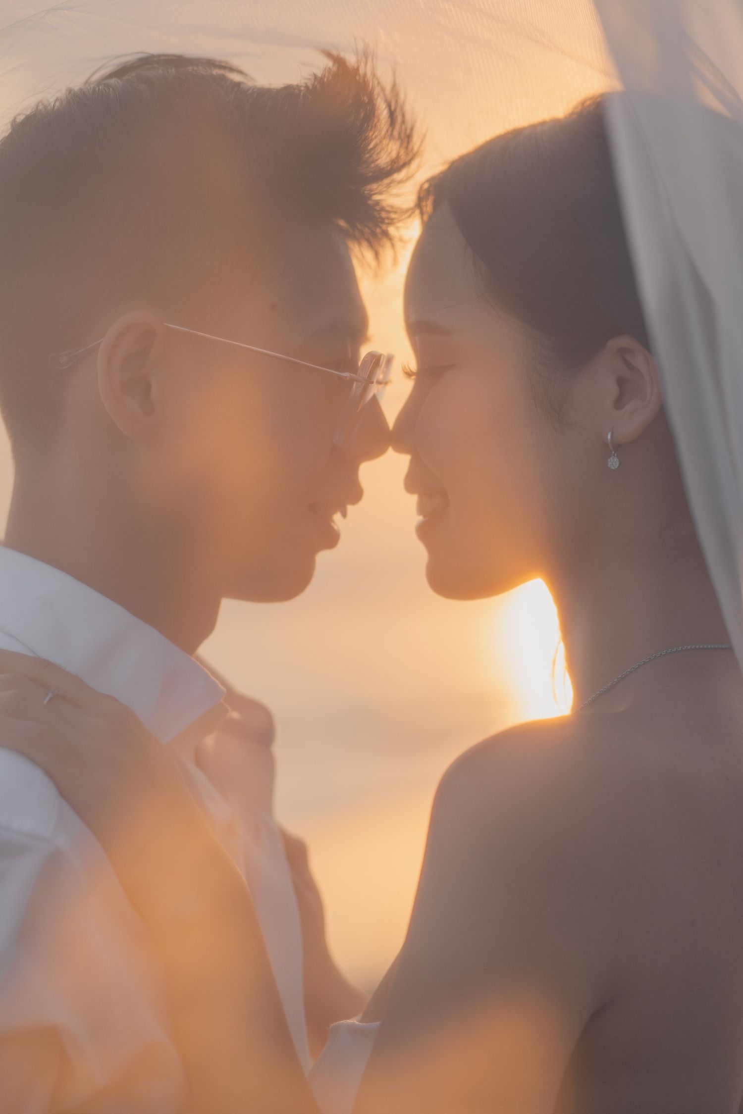 Romantic couple sharing an intimate moment under a veil at golden hour sunset, wedding photography.