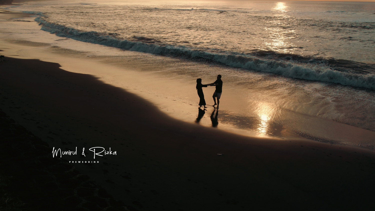 Silhouette of a couple holding hands on a beach at sunset with golden reflections on the water.