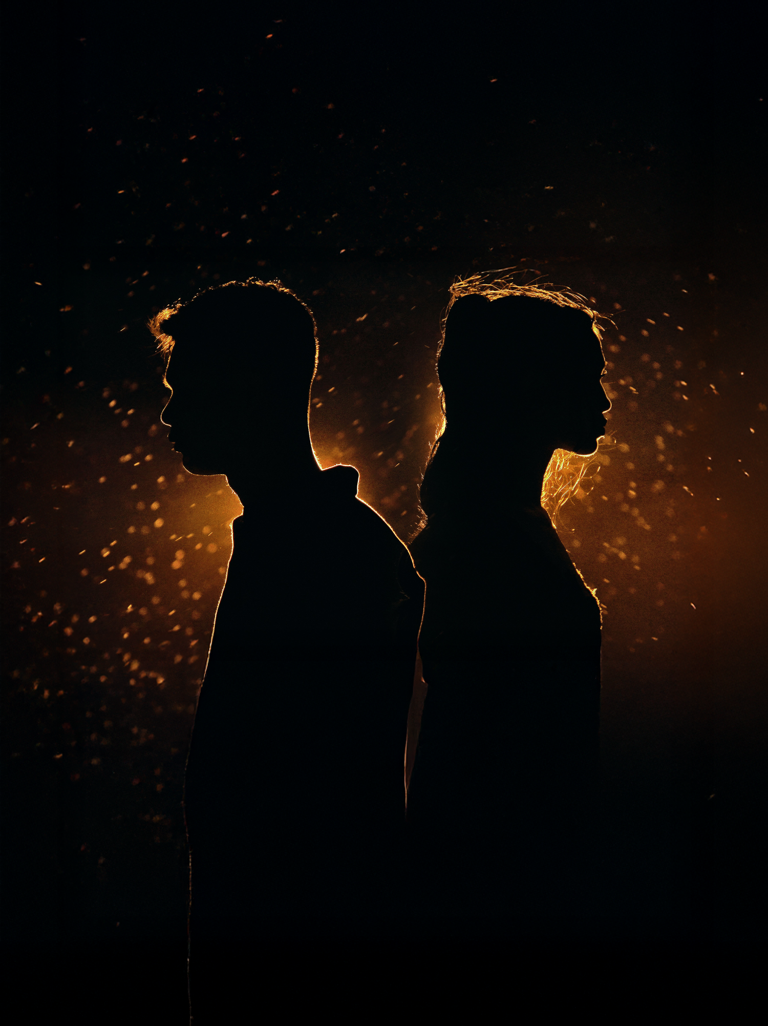 Two silhouettes back-to-back against a dark background with glowing golden sparks and light between them.