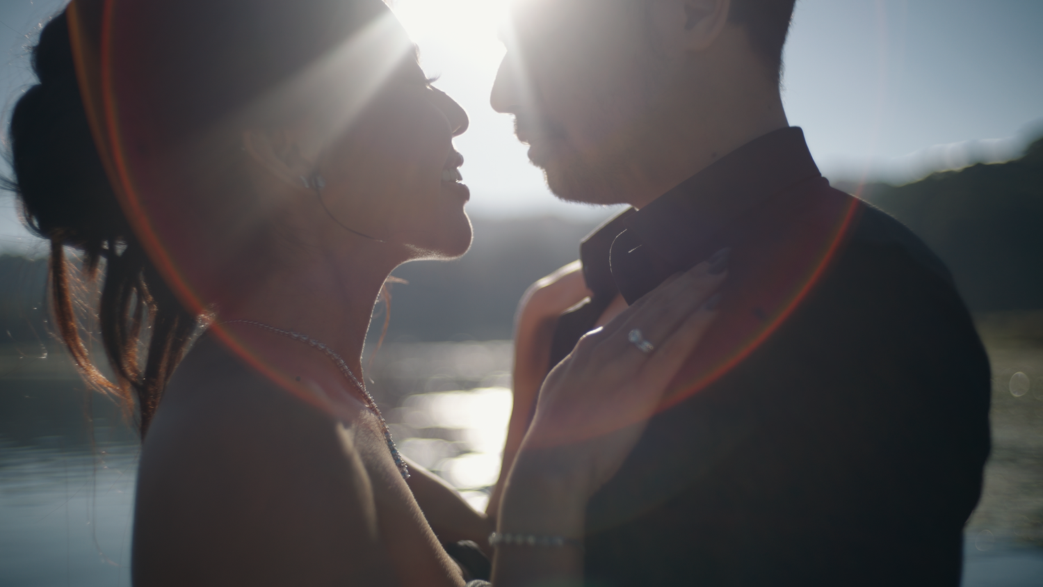 Romantic couple sharing an intimate moment backlit by golden sunlight near a serene lake.