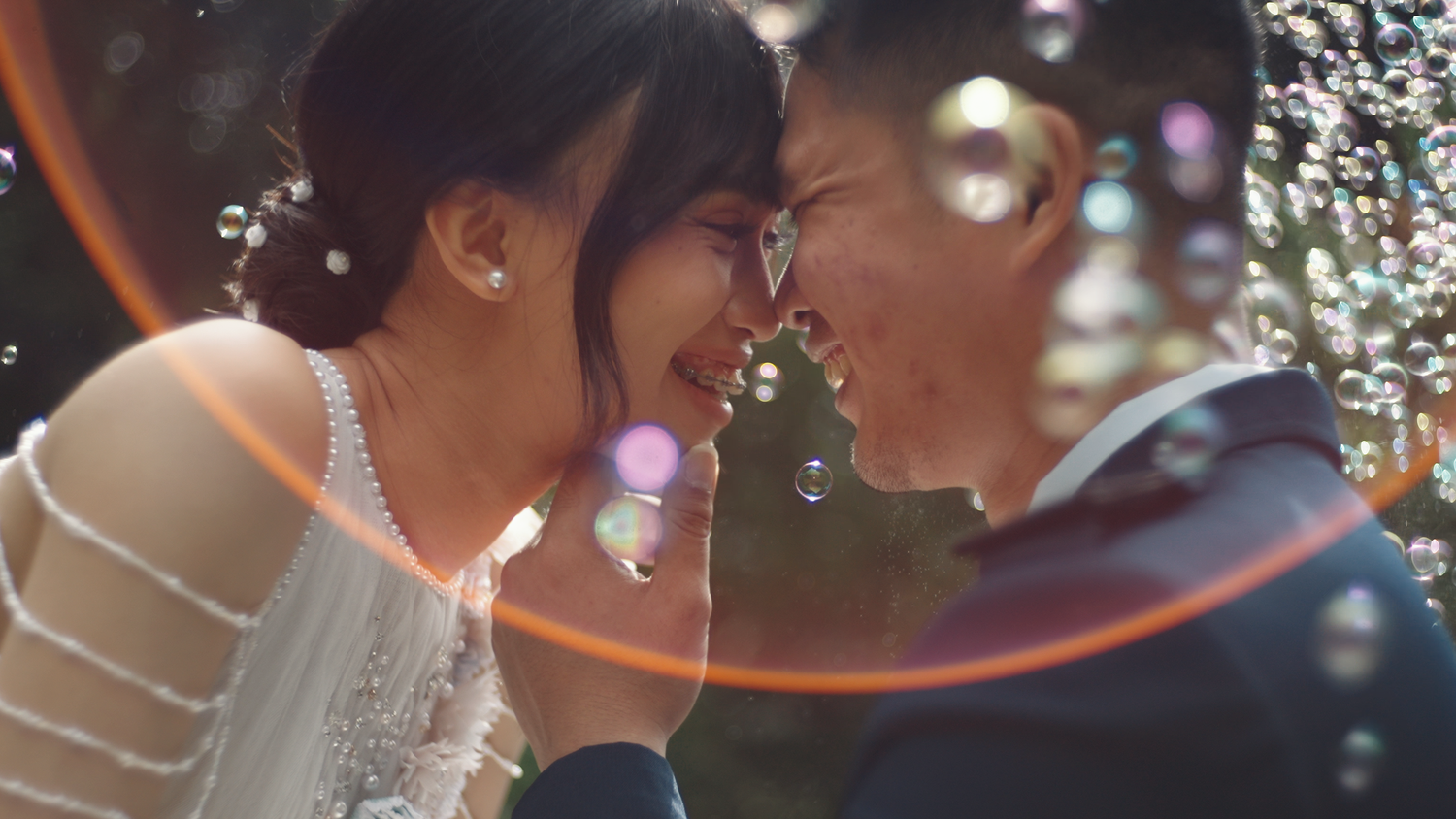 A joyful couple shares an intimate moment surrounded by bubbles, touching foreheads and smiling on their wedding day.