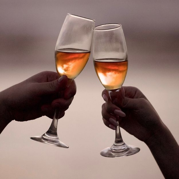Two hands clinking glasses of rose wine in a celebratory toast against a soft blurred background.