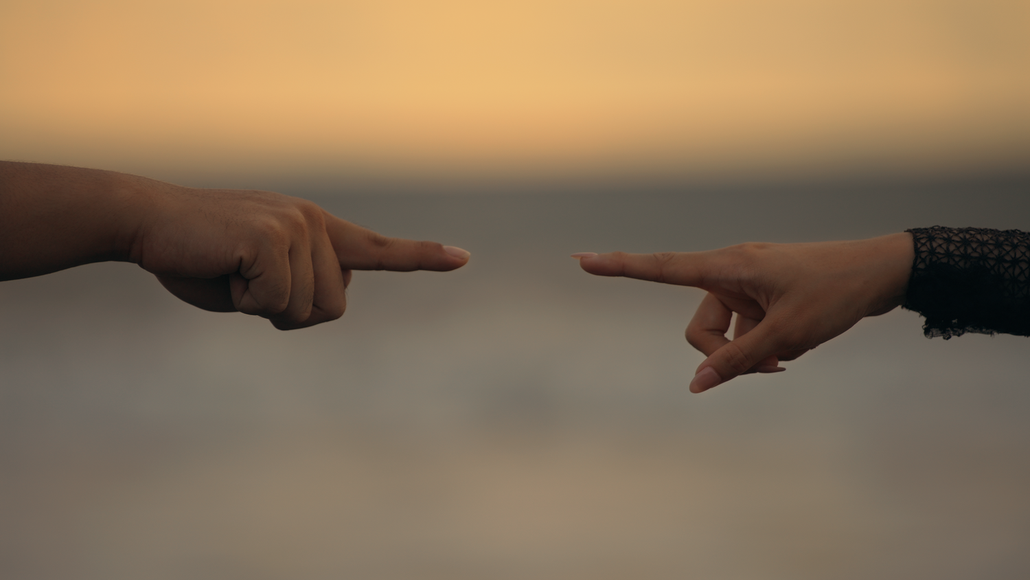 Two hands pointing at each other against a golden sunset sky background.