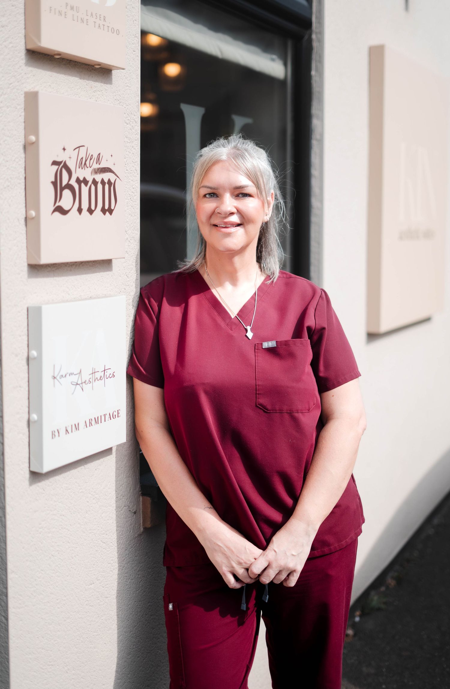 Female beauty professional in burgundy scrubs standing outside Jules Brow studio signage.