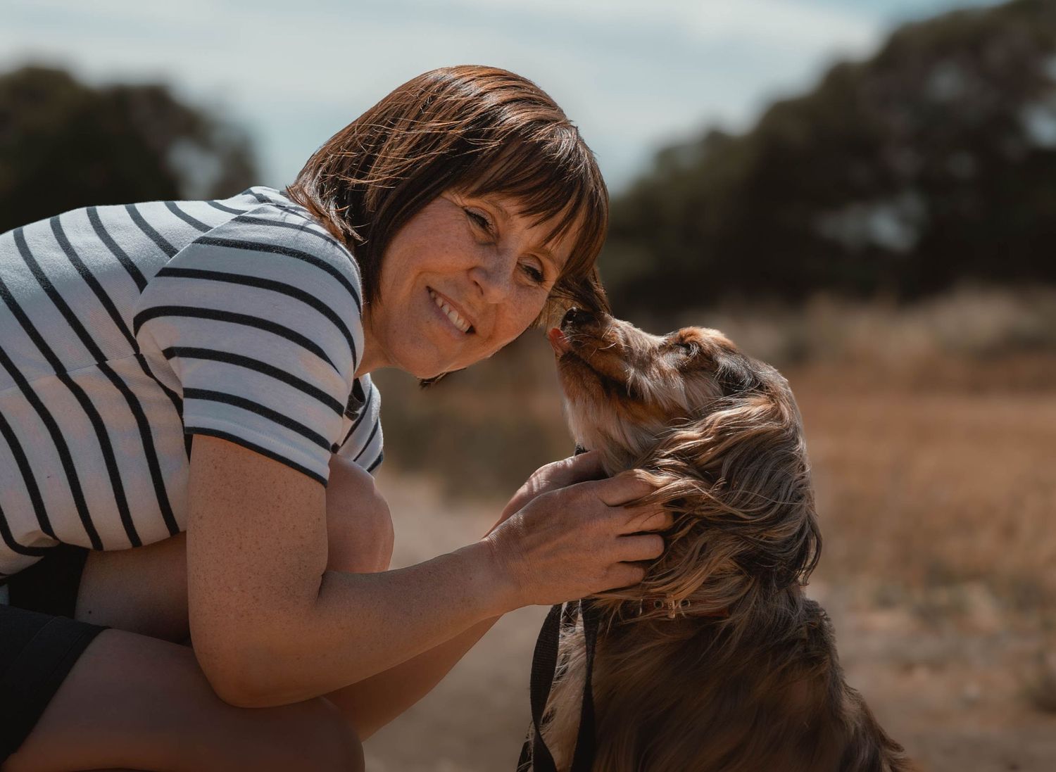Smiling woman with short hair petting and bonding with a Golden Retriever dog outdoors.