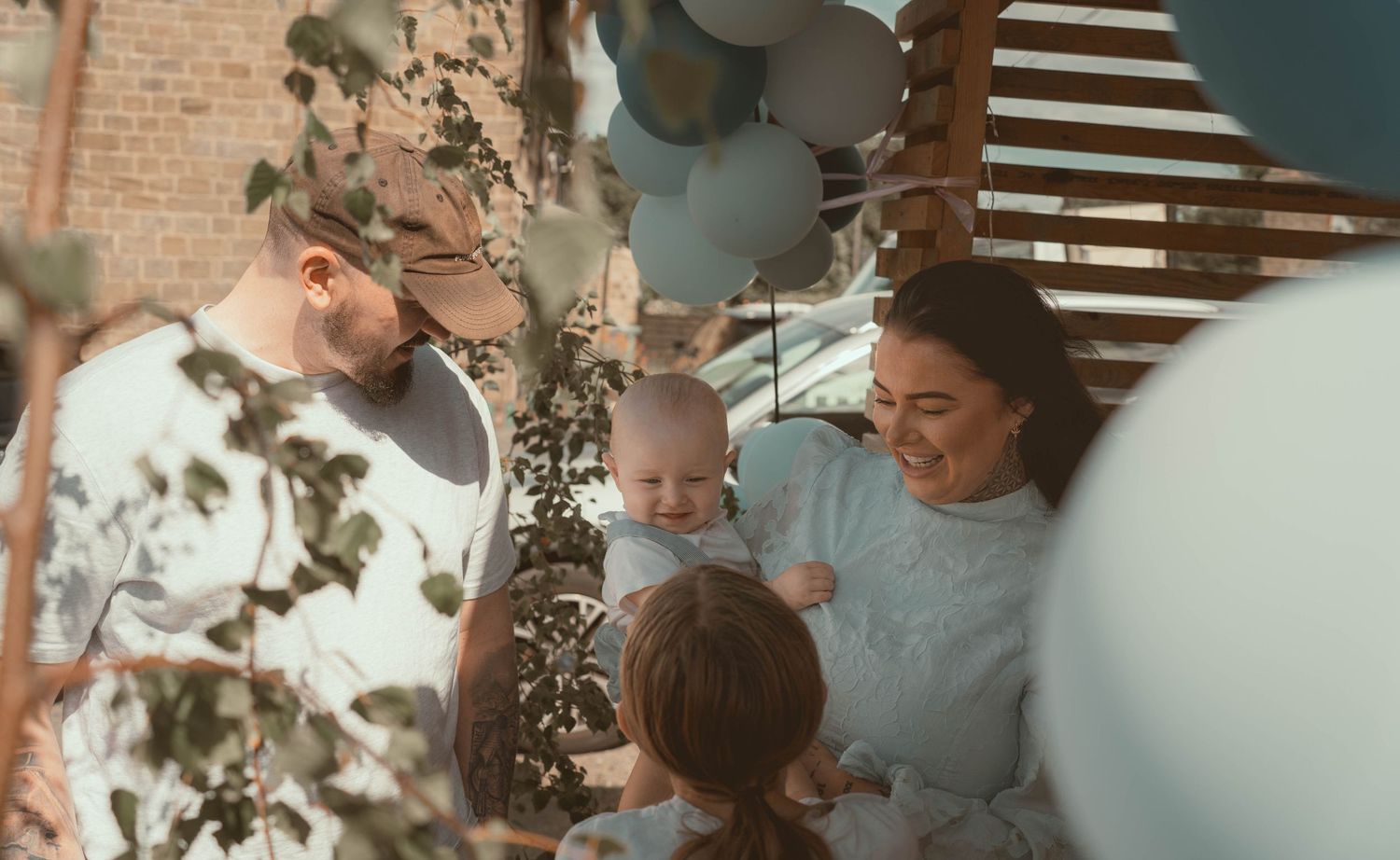 A happy family with a baby celebrates surrounded by blue and white balloons in a decorated space.