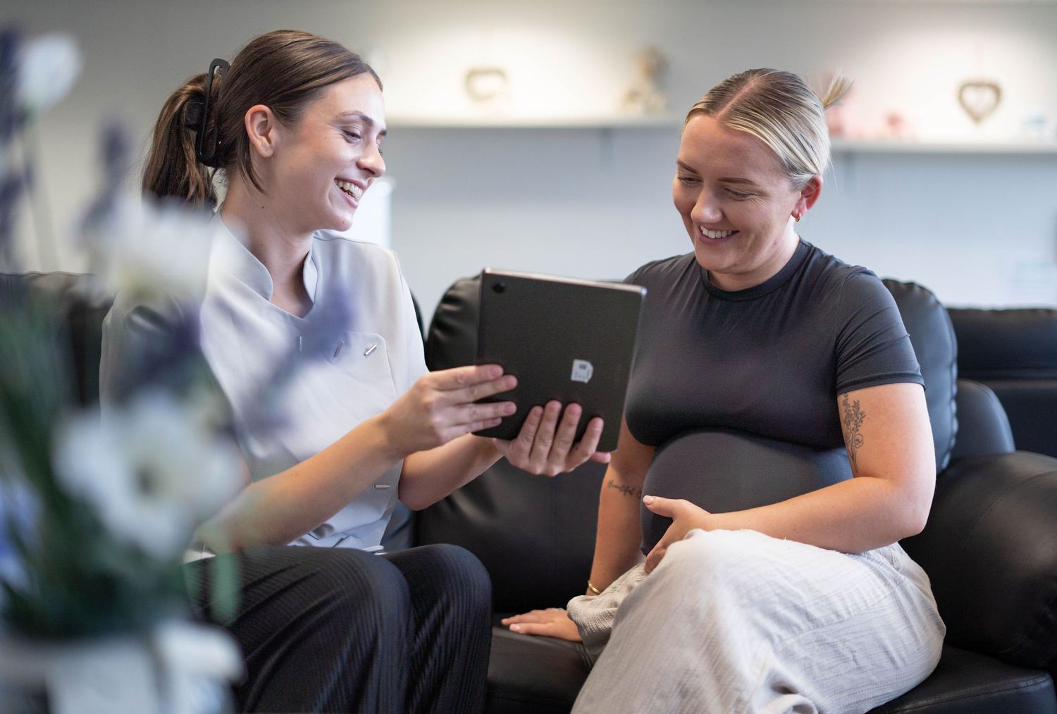 A healthcare professional and pregnant woman smile while reviewing information on a tablet together.