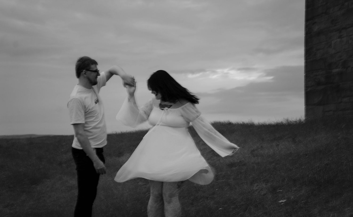 Black and white photo of couple dancing outdoors, woman in white dress spinning gracefully.