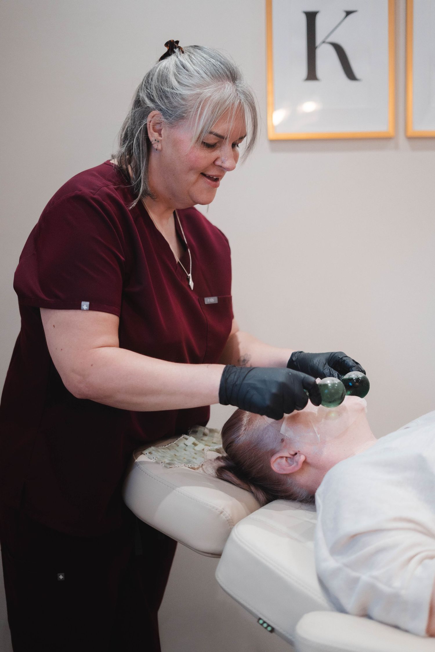 Beauty professional in black gloves performing facial treatment with jade roller on client.