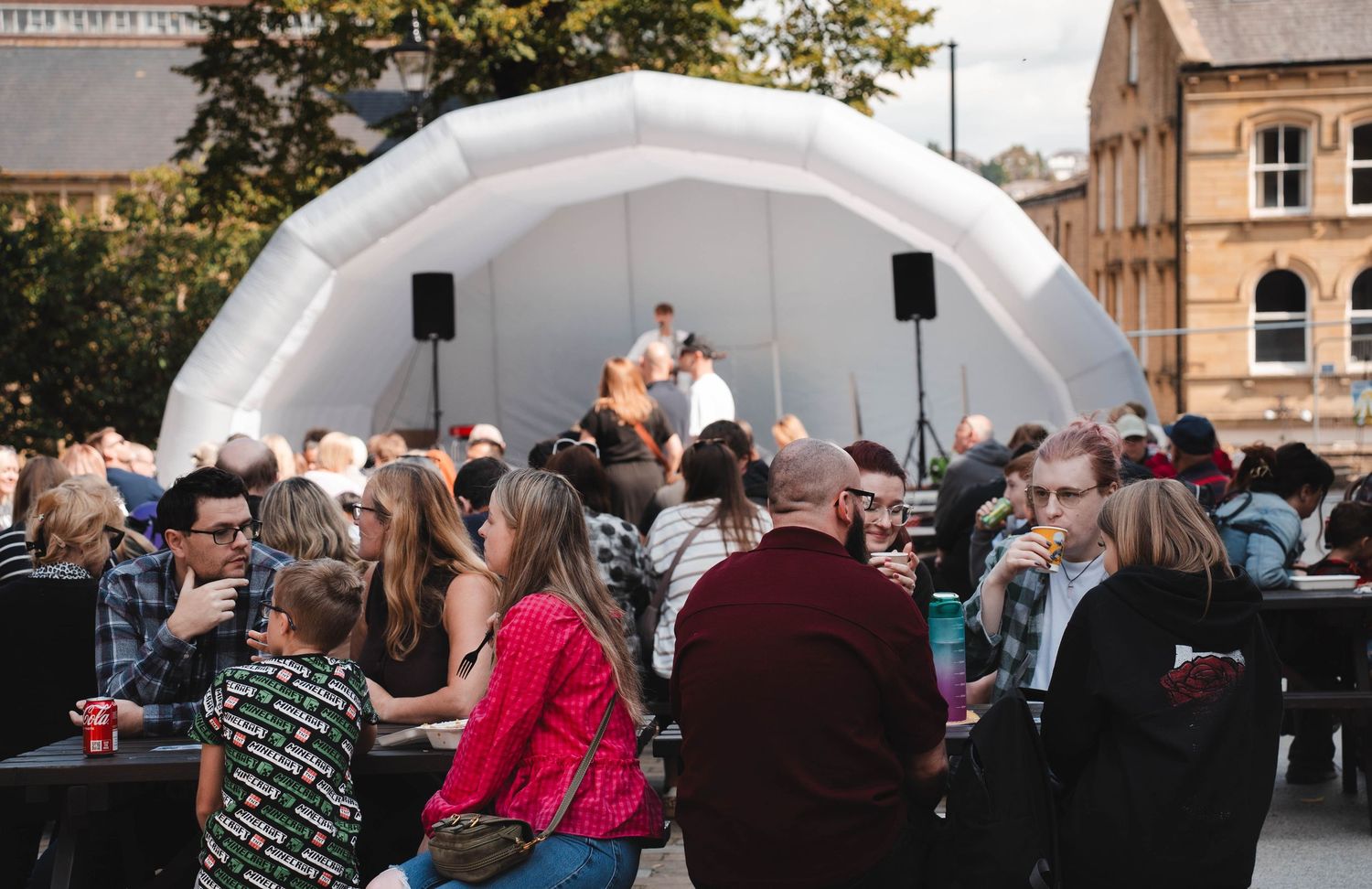 Crowd of people gathered at an outdoor community event under an inflatable stage canopy.