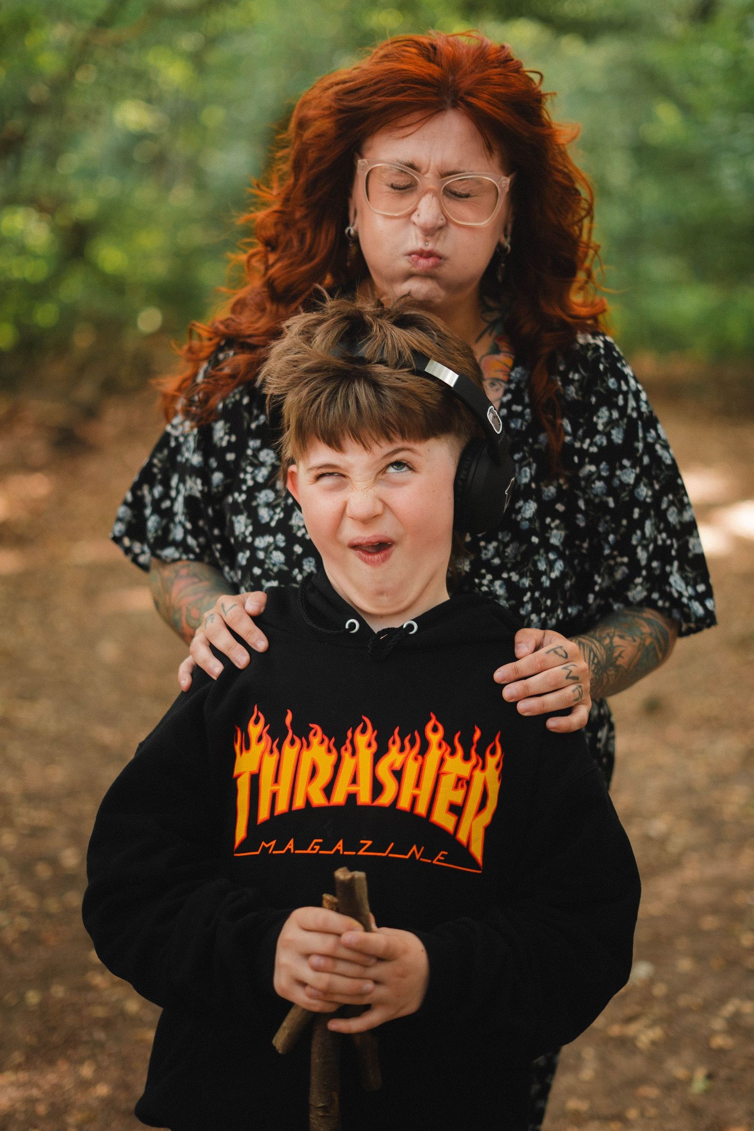 Red-haired woman and child in Thrasher hoodie making funny faces together in a forest path.