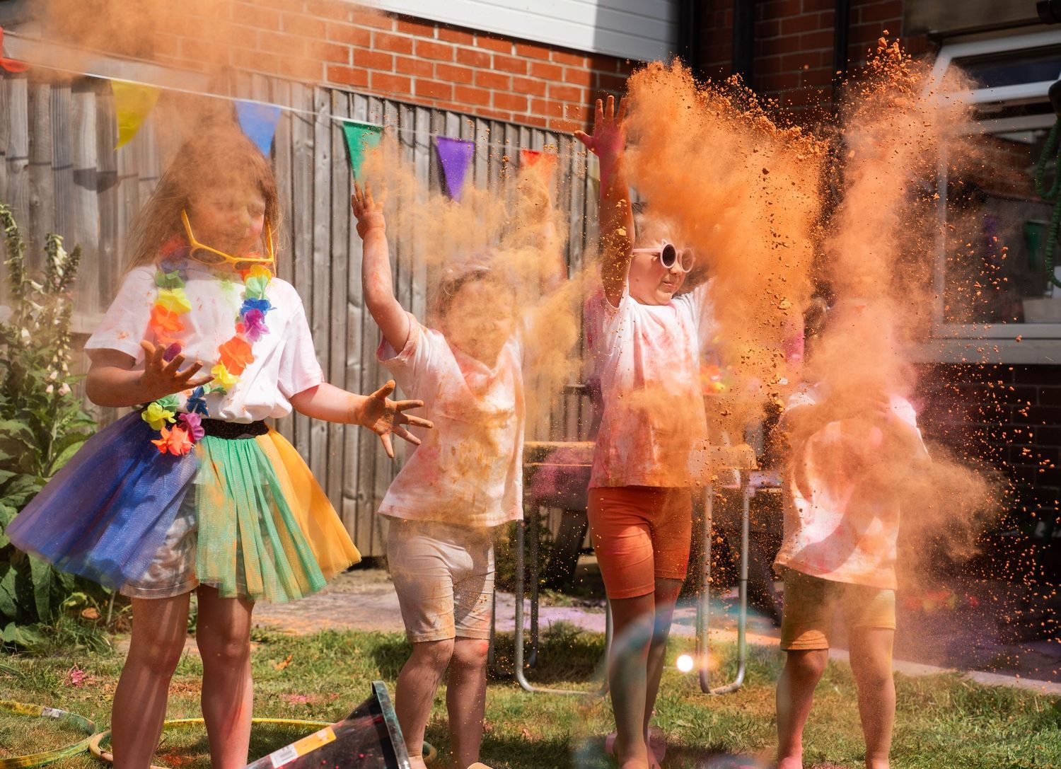 Family throwing vibrant orange Holi color powder in a sunny backyard celebration together.