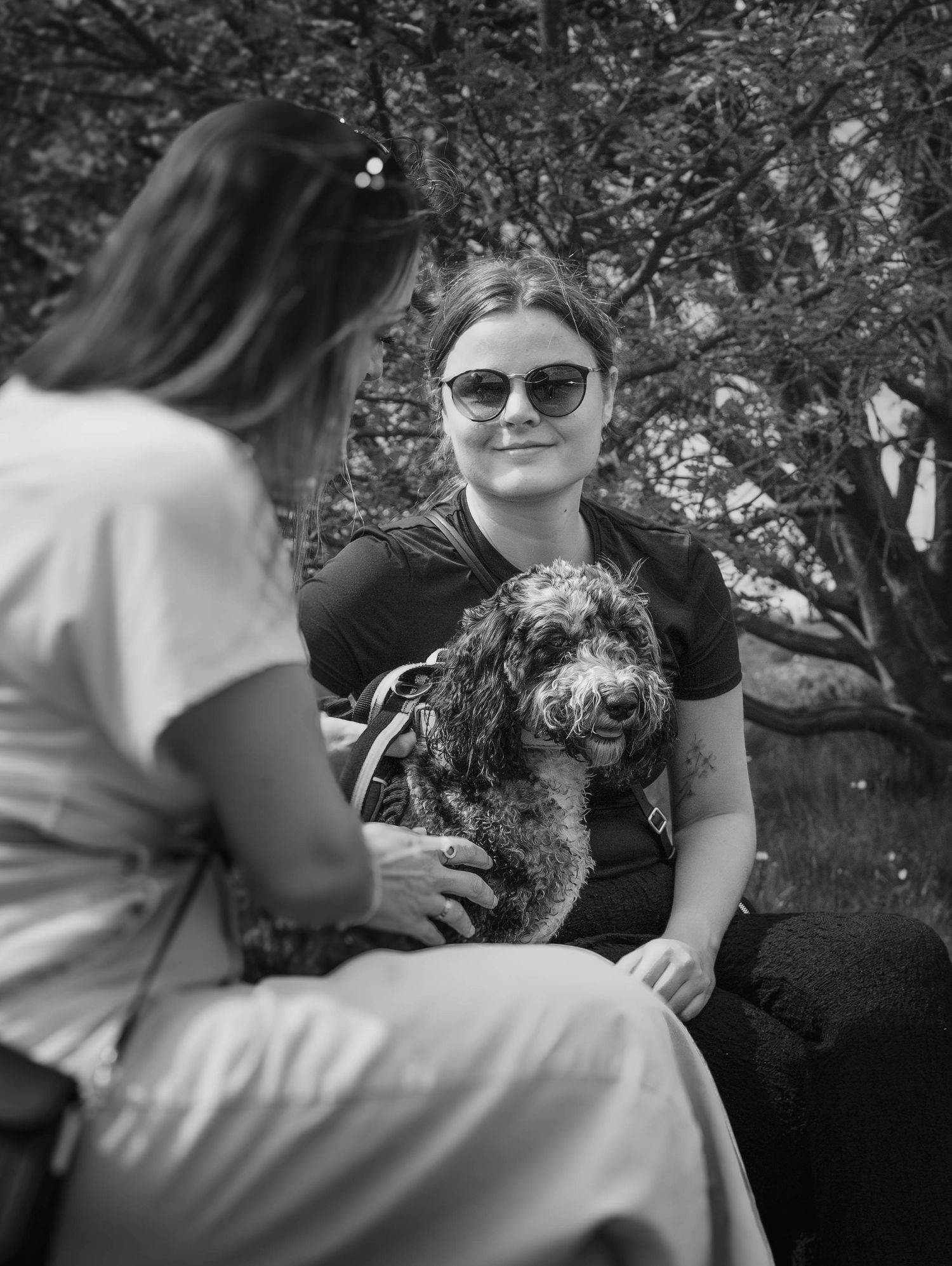 Woman holding a curly dog while another woman visits in black and white photo.