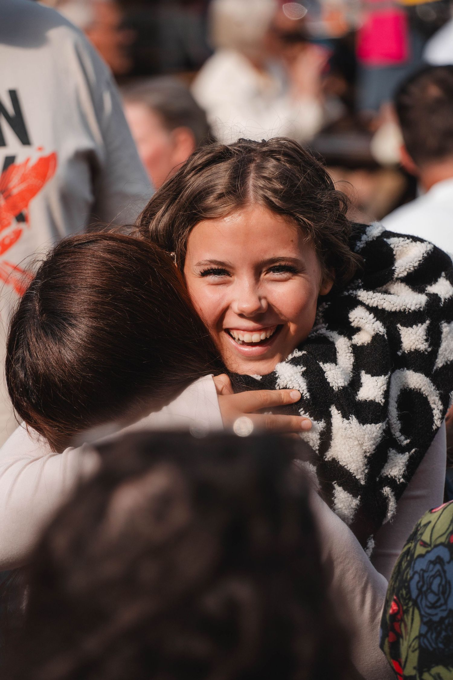 Young girl smiling joyfully while being embraced at an outdoor event.