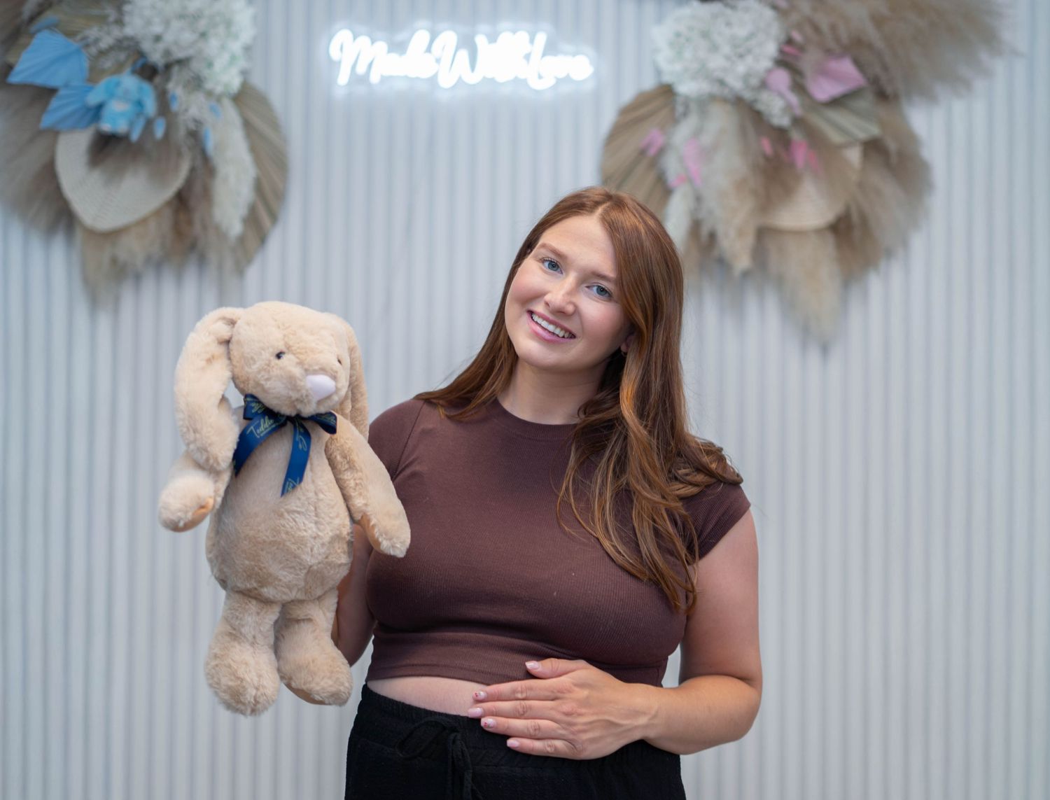 Smiling pregnant woman holding a stuffed bunny toy in a decorated studio setting.