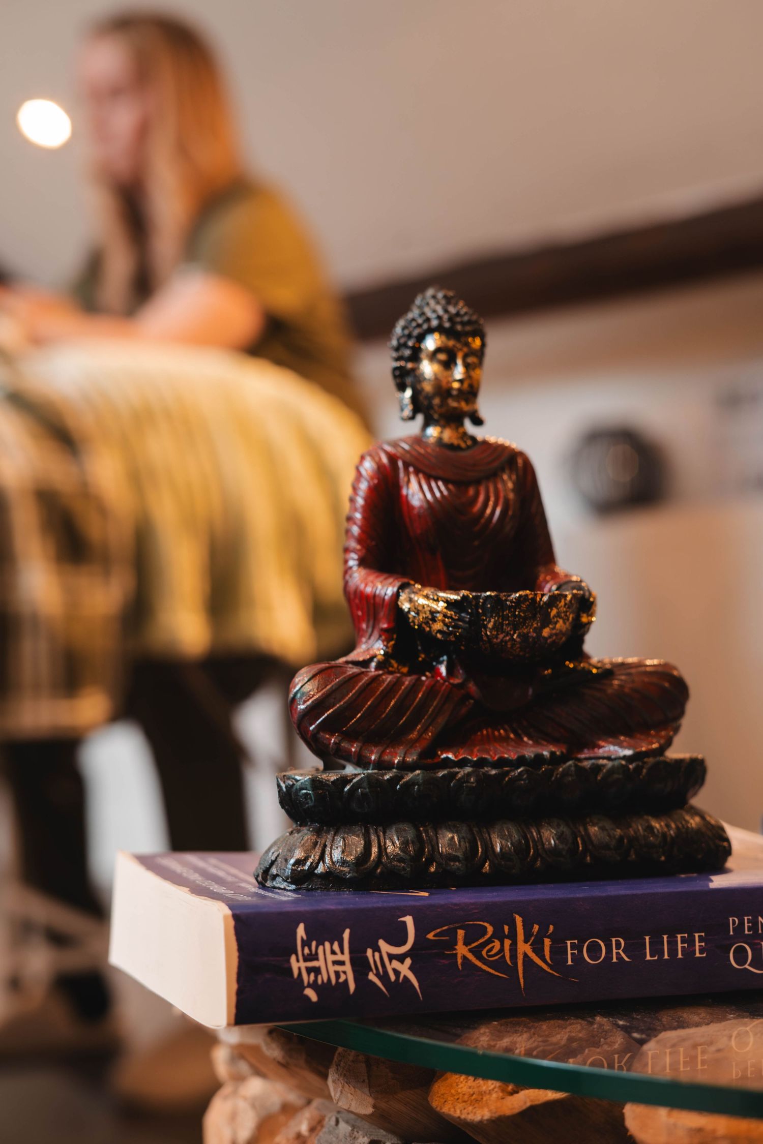 Red Buddha figurine sitting atop Reiki for Life books in a serene wellness treatment room.