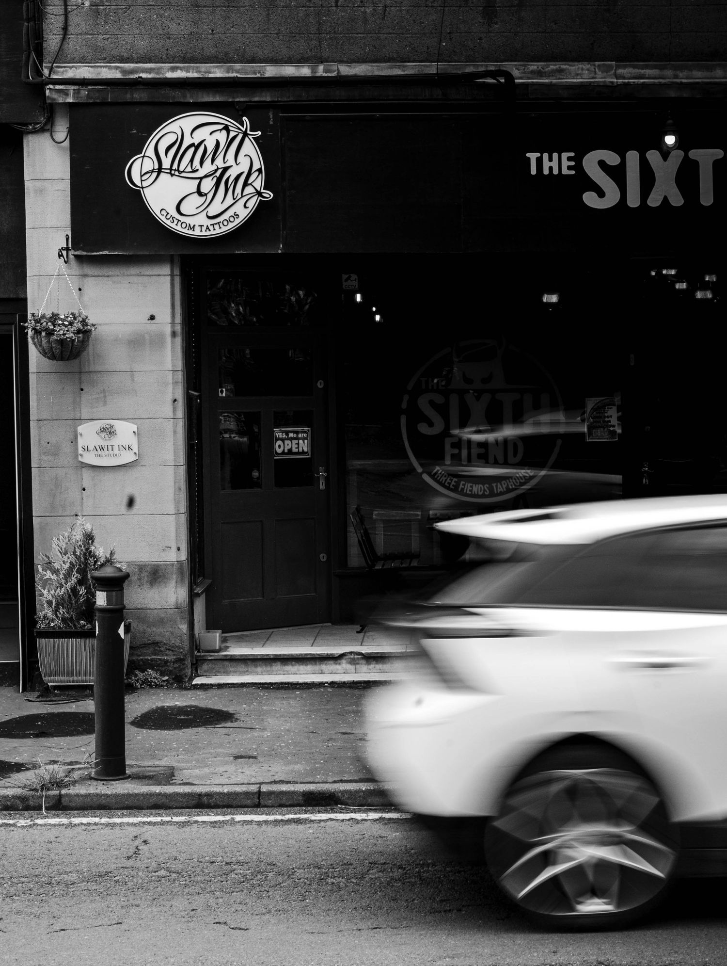 Black and white photo of Slant Ink tattoo studio storefront with a car passing by.