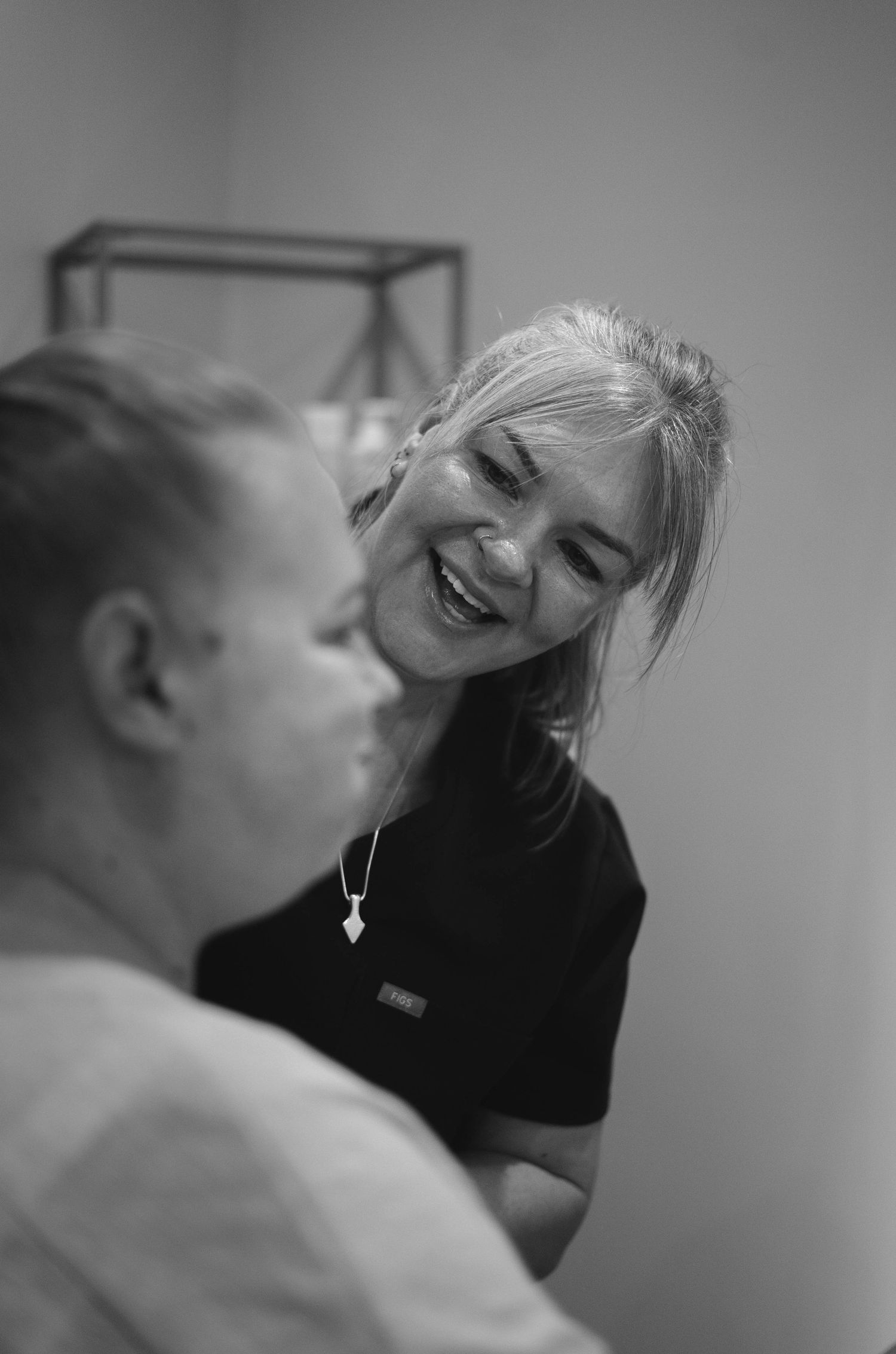 Black and white photo of smiling beauty therapist engaging warmly with seated client.