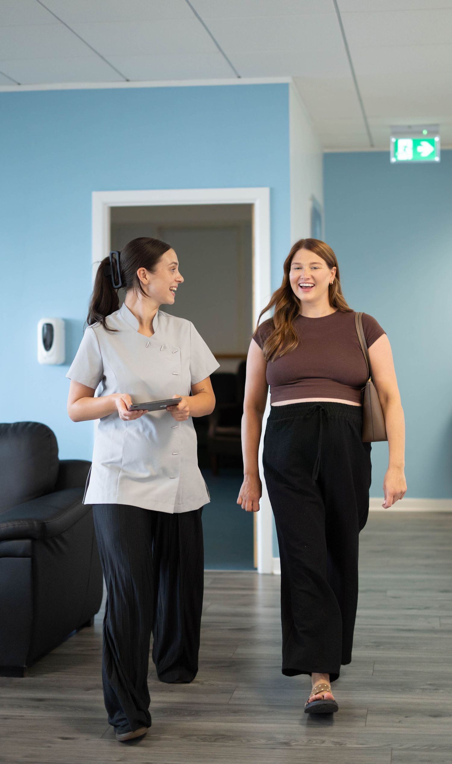 Smiling healthcare professional walks alongside laughing pregnant patient in a modern clinic.
