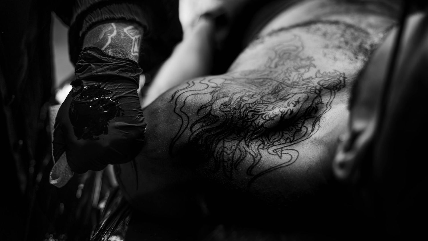 Black and white close-up of a tattoo artist applying intricate flame designs to a clients arm.