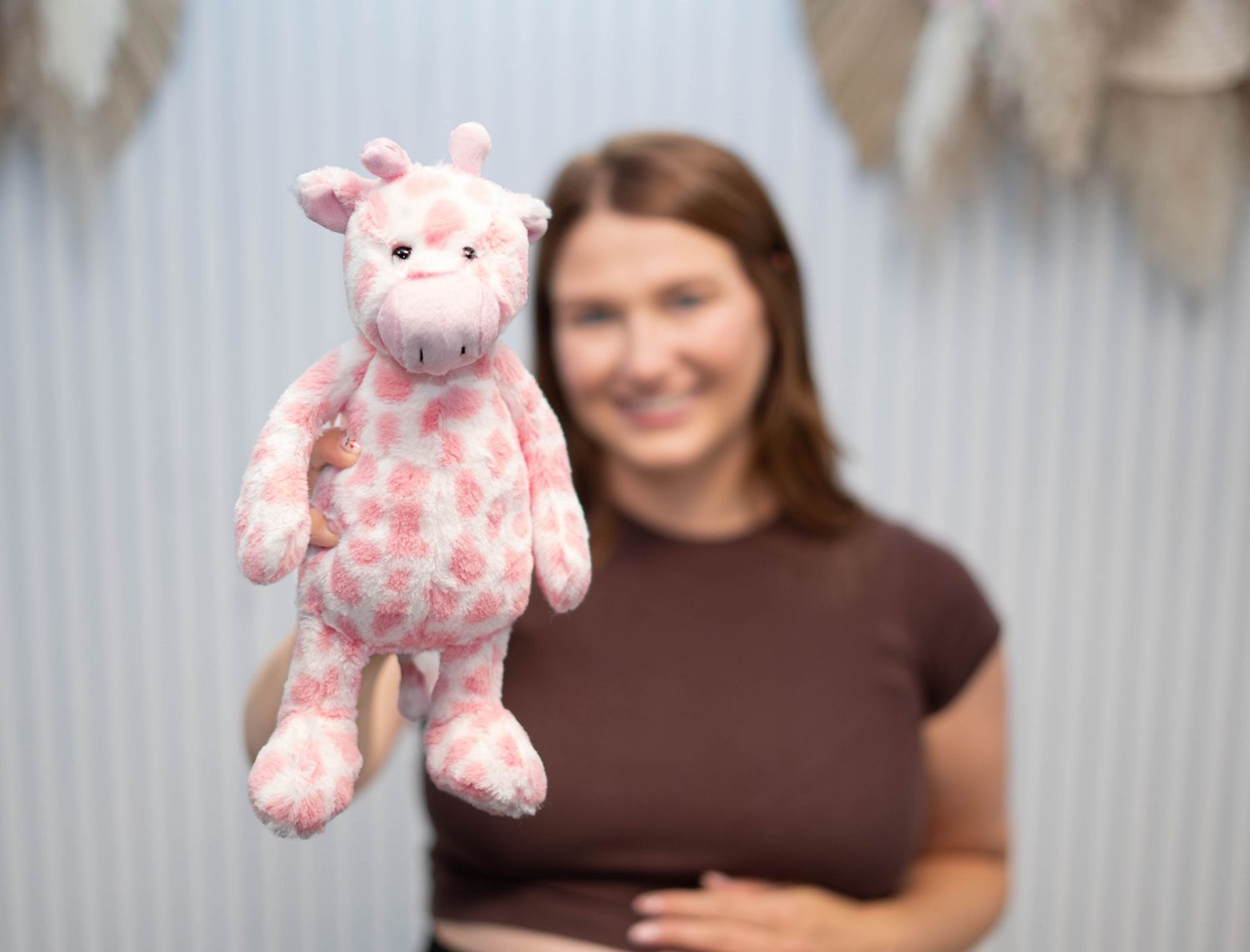 Smiling pregnant woman holds up a pink giraffe stuffed animal toy in a decorated nursery.