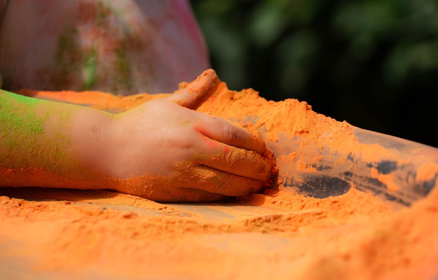 Child's hand covered in bright orange Holi powder pressed against a colorful powder-covered surface.