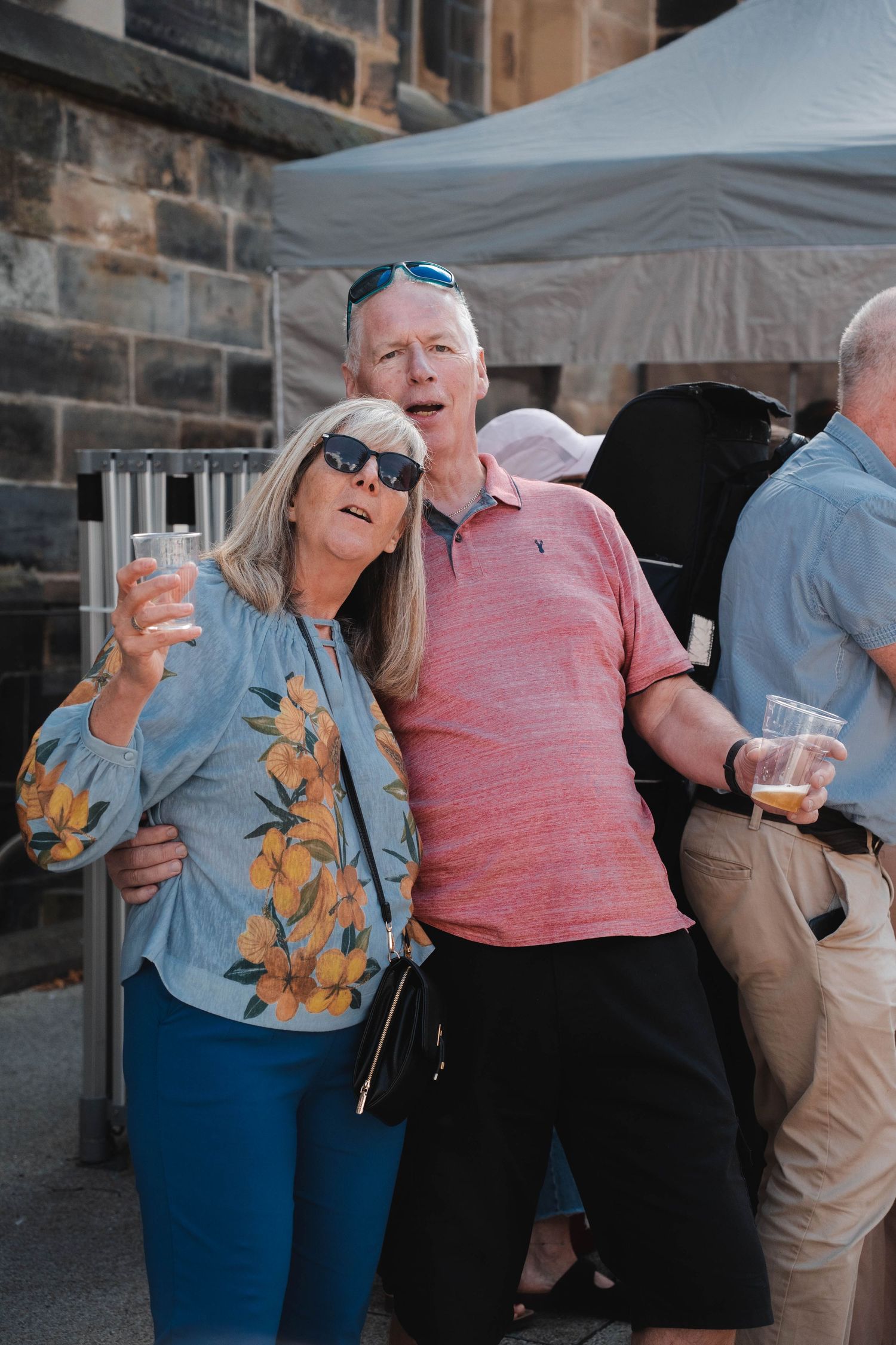 Older couple holding drinks and posing together at an outdoor festival event.