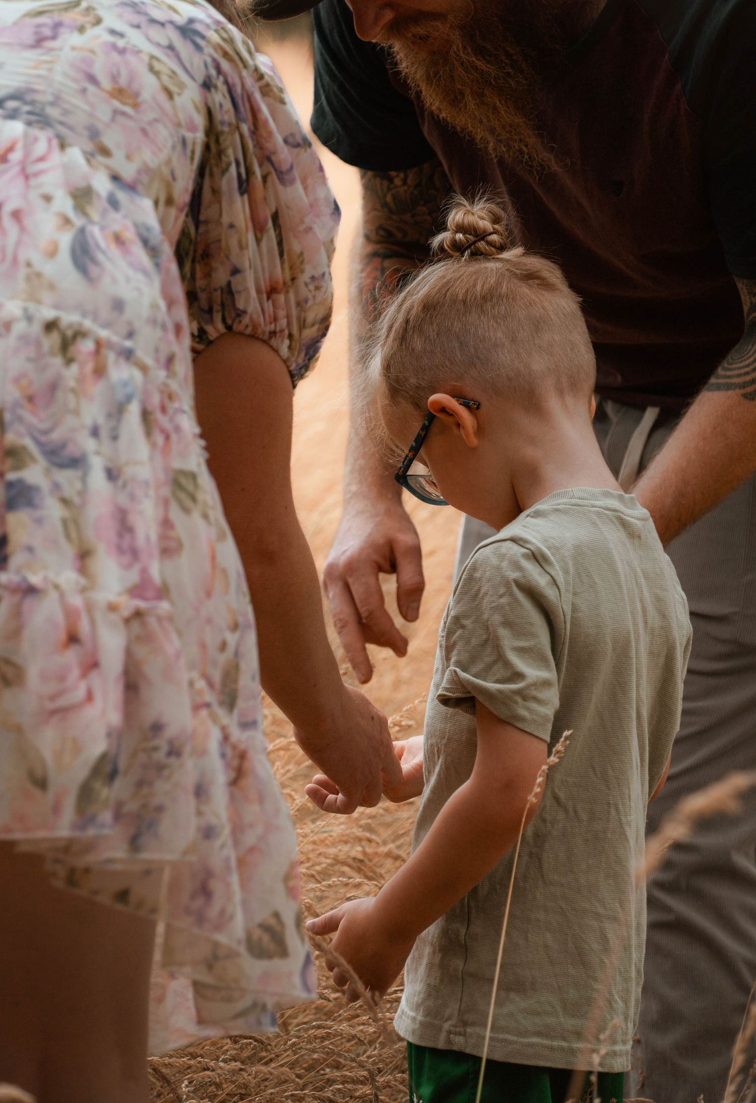 Young child with hearing aid and glasses holds an adult's hand while exploring outdoors.