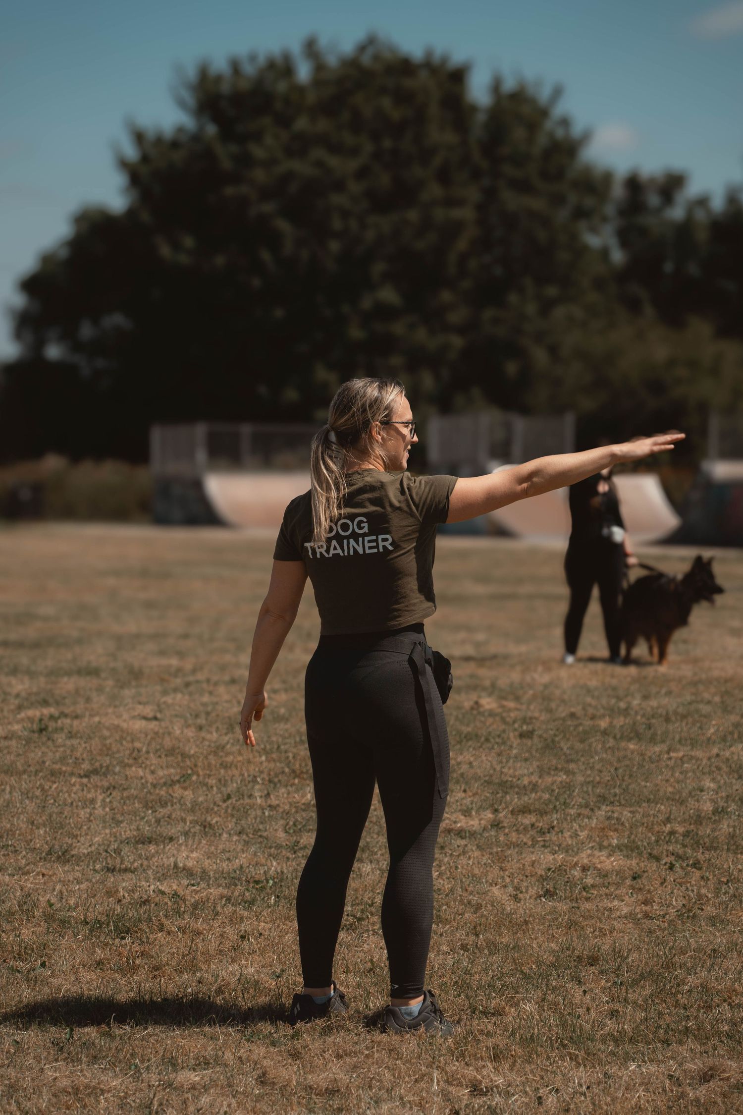 Female dog trainer in black t-shirt pointing in an outdoor training field.