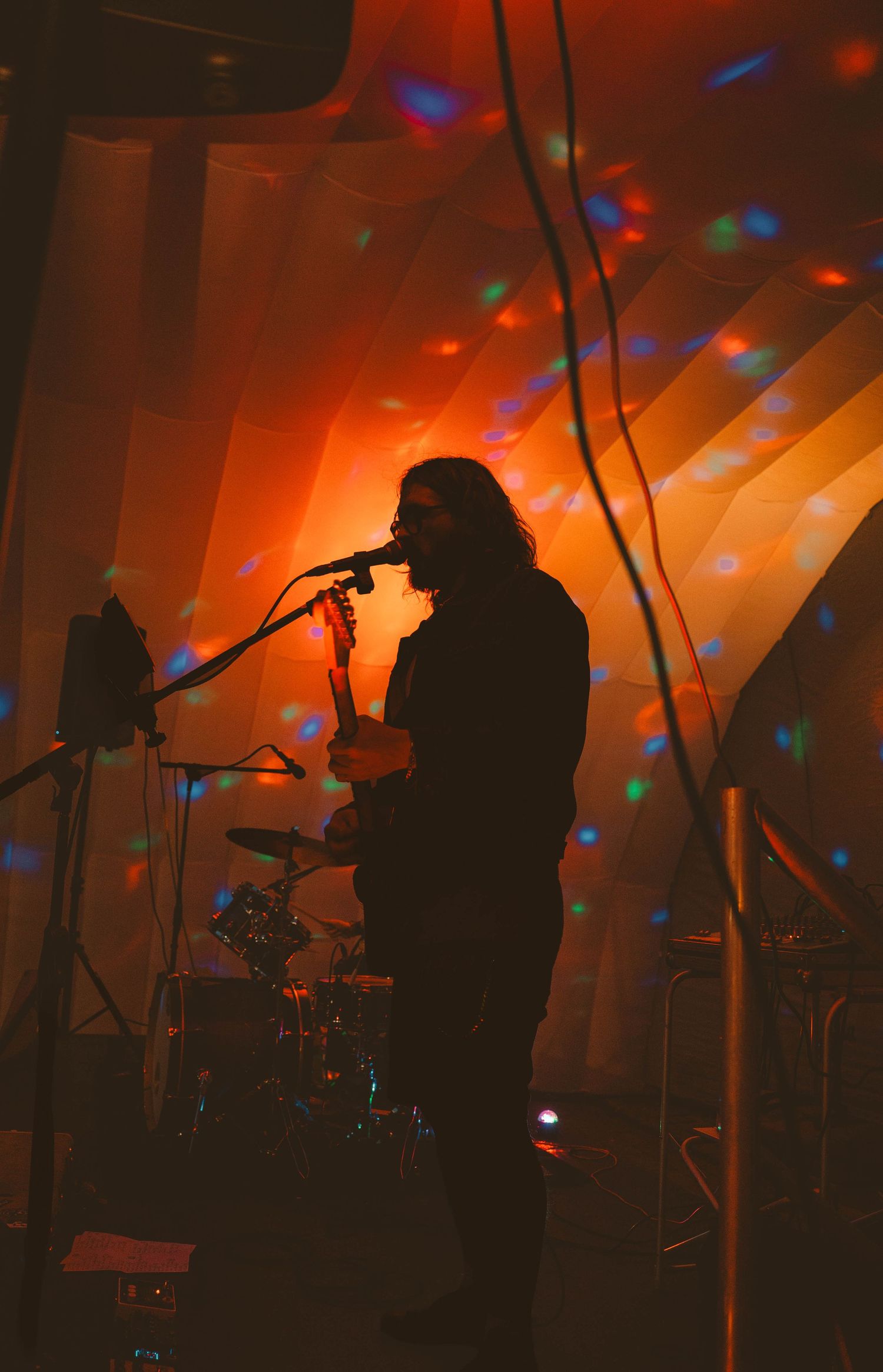 Silhouetted guitarist performing on stage with colorful disco lights and orange backdrop.