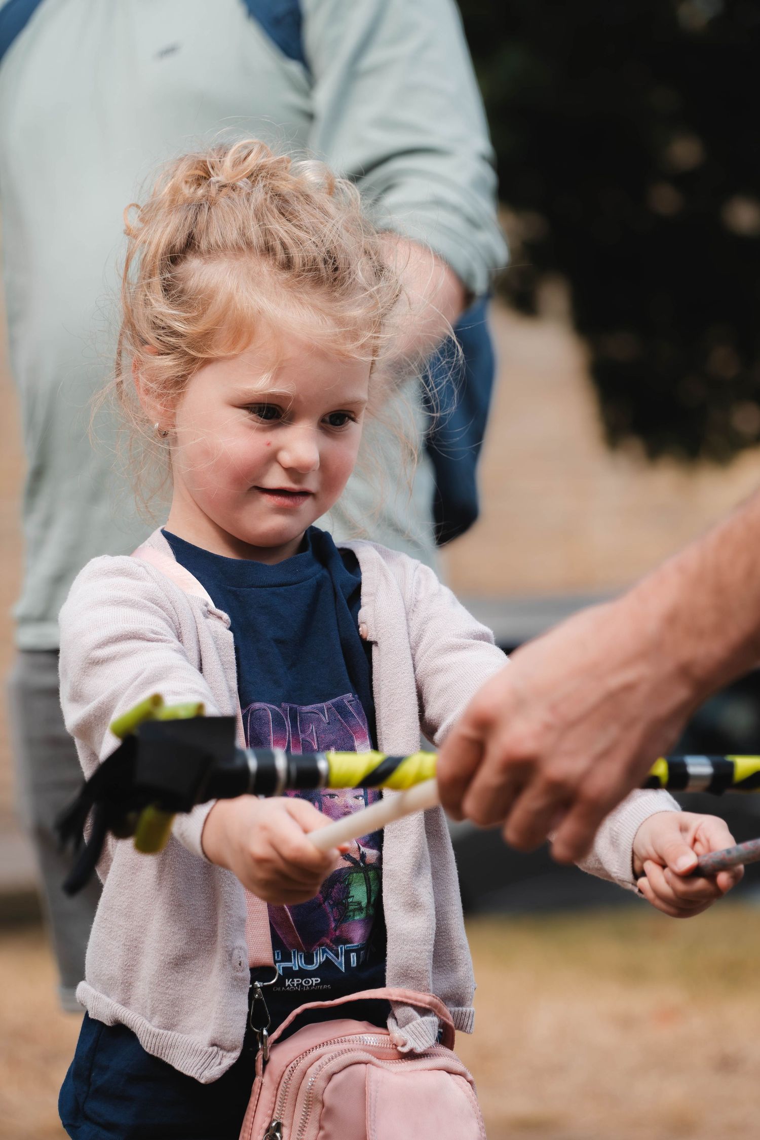 A young blonde girl holds juggling sticks at an outdoor festival event.