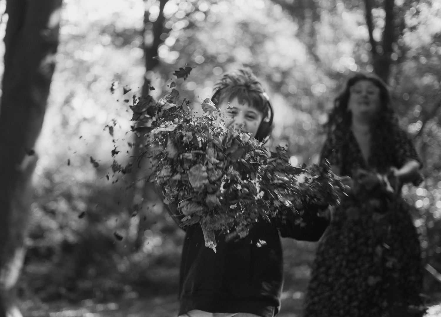 Black and white photo of a child throwing leaves in the air in a forest.