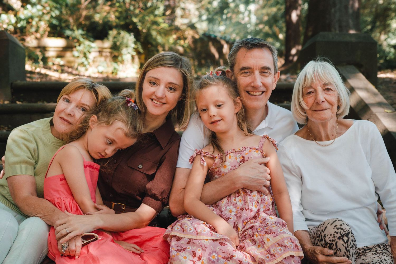 Happy multi-generational family of six smiling together outdoors in a lush garden setting.