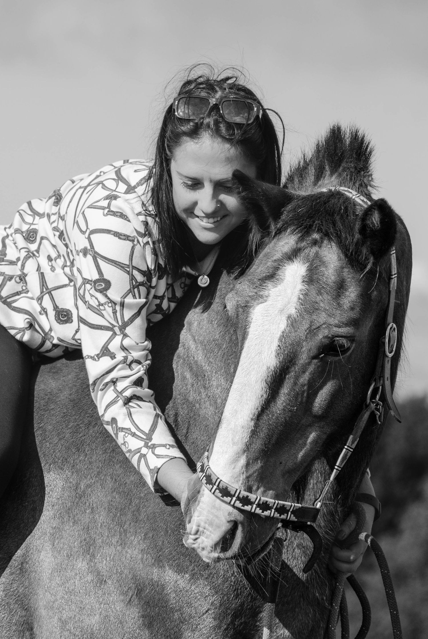 A smiling dark-haired woman leans forward to affectionately nuzzle a horse in black and white.