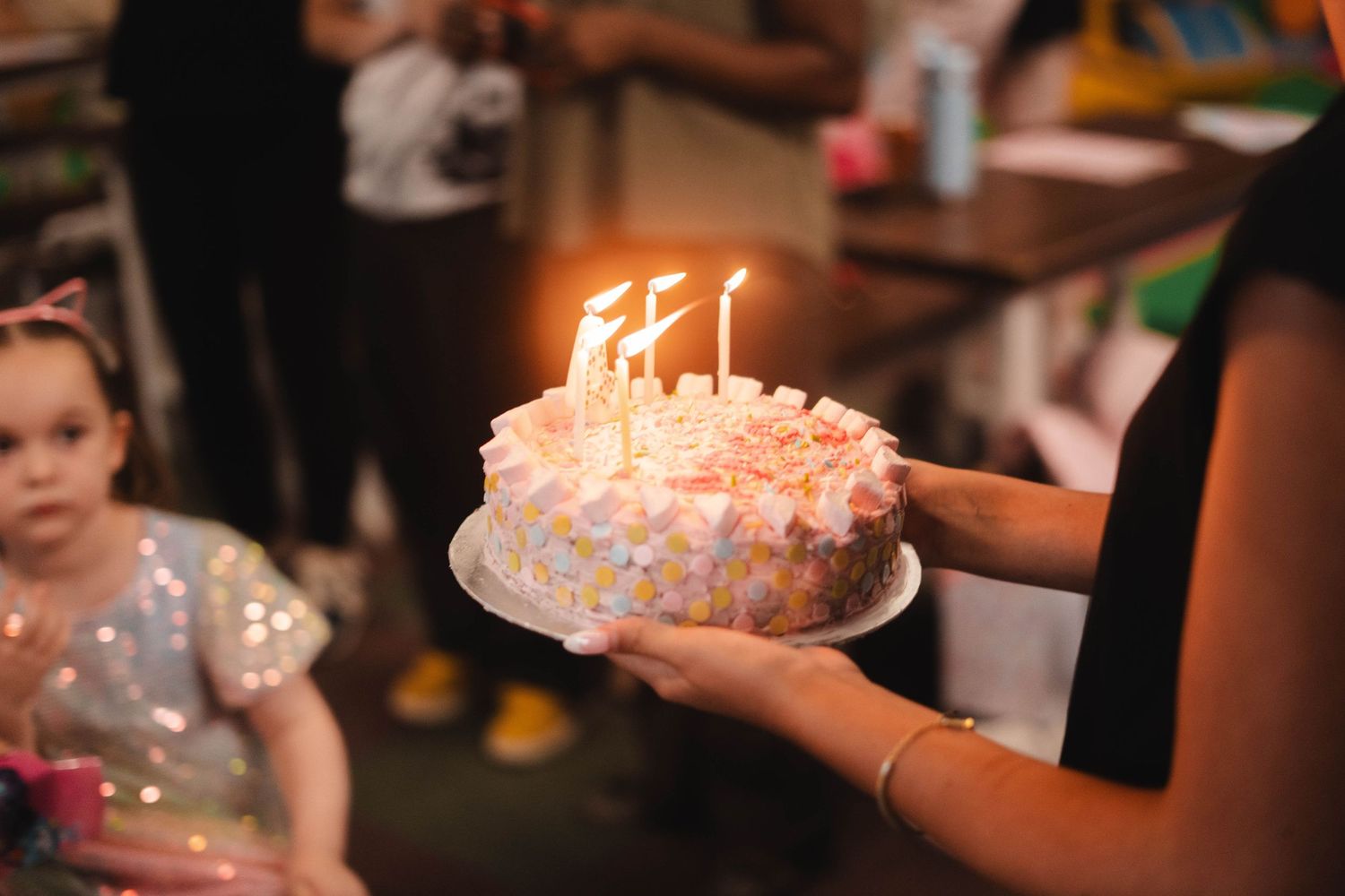 Person holding birthday cake with lit candles at a childrens birthday party.