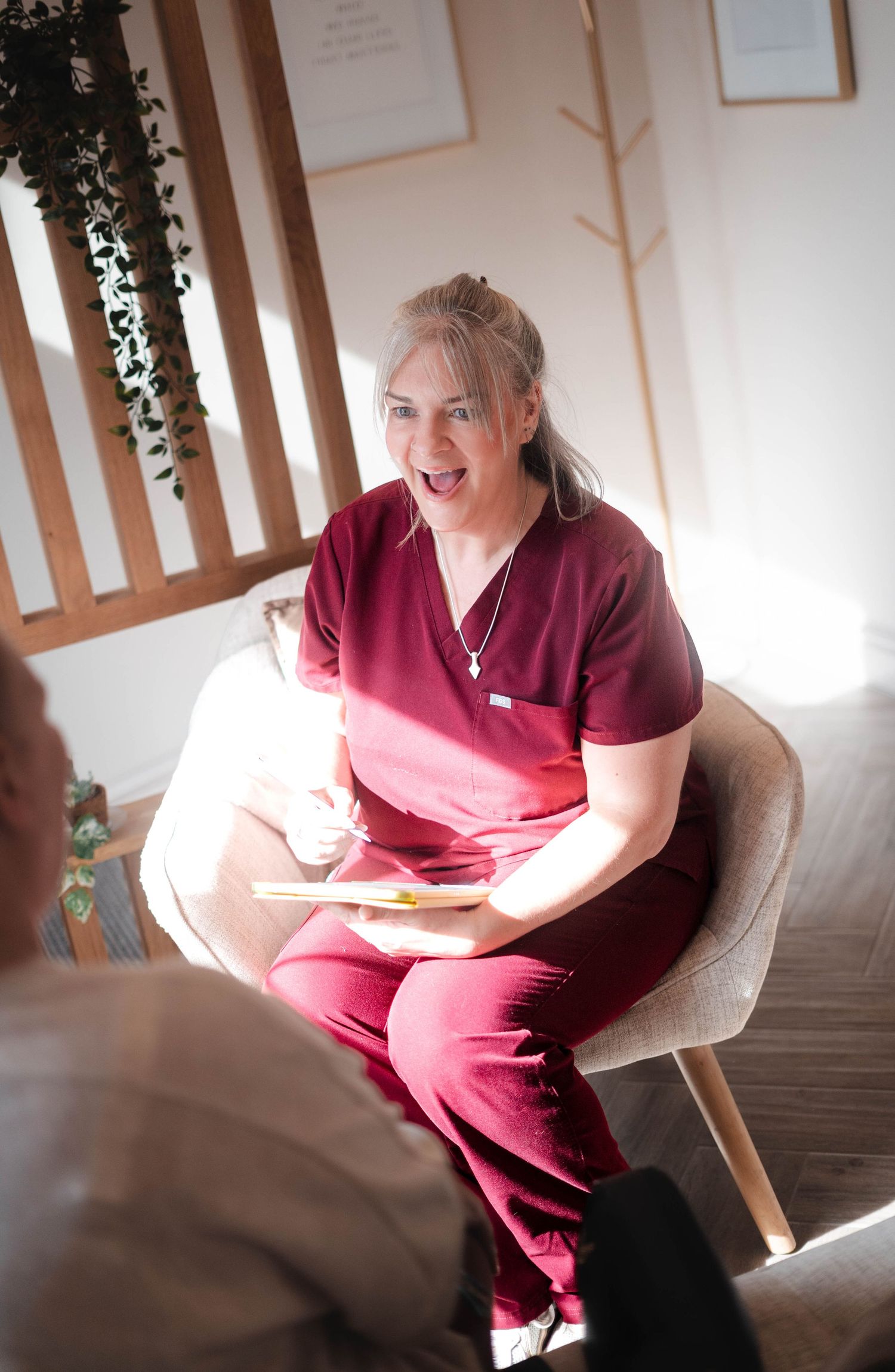 Female healthcare professional in burgundy scrubs smiling during patient consultation in modern clinic.