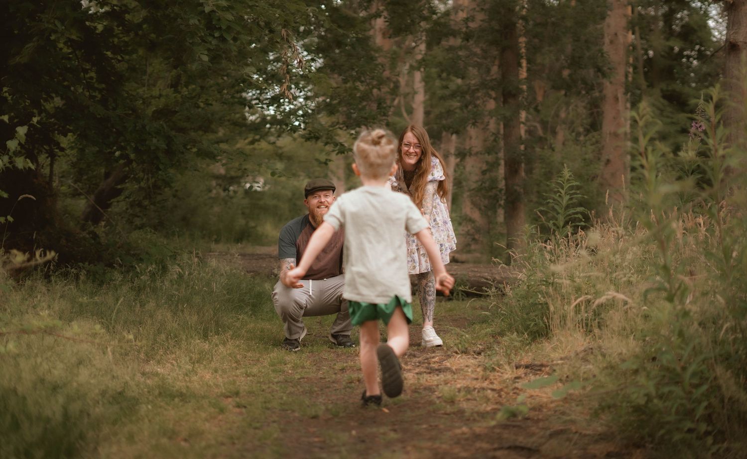 Young girl running toward her parents along a forest path in a candid family photography session.