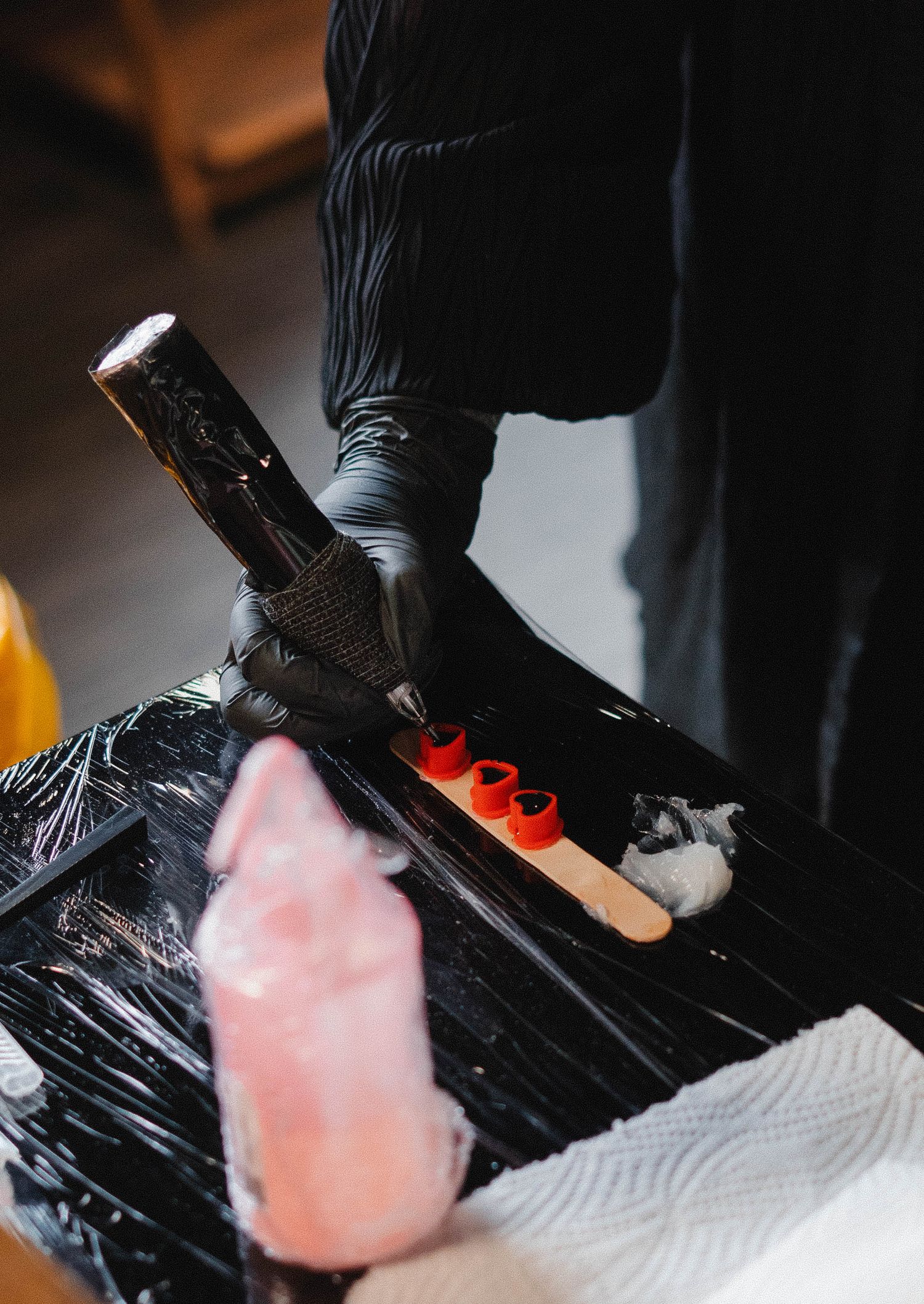 Tattoo artist in black gloves preparing ink colors on a wrapped station before a tattooing session.